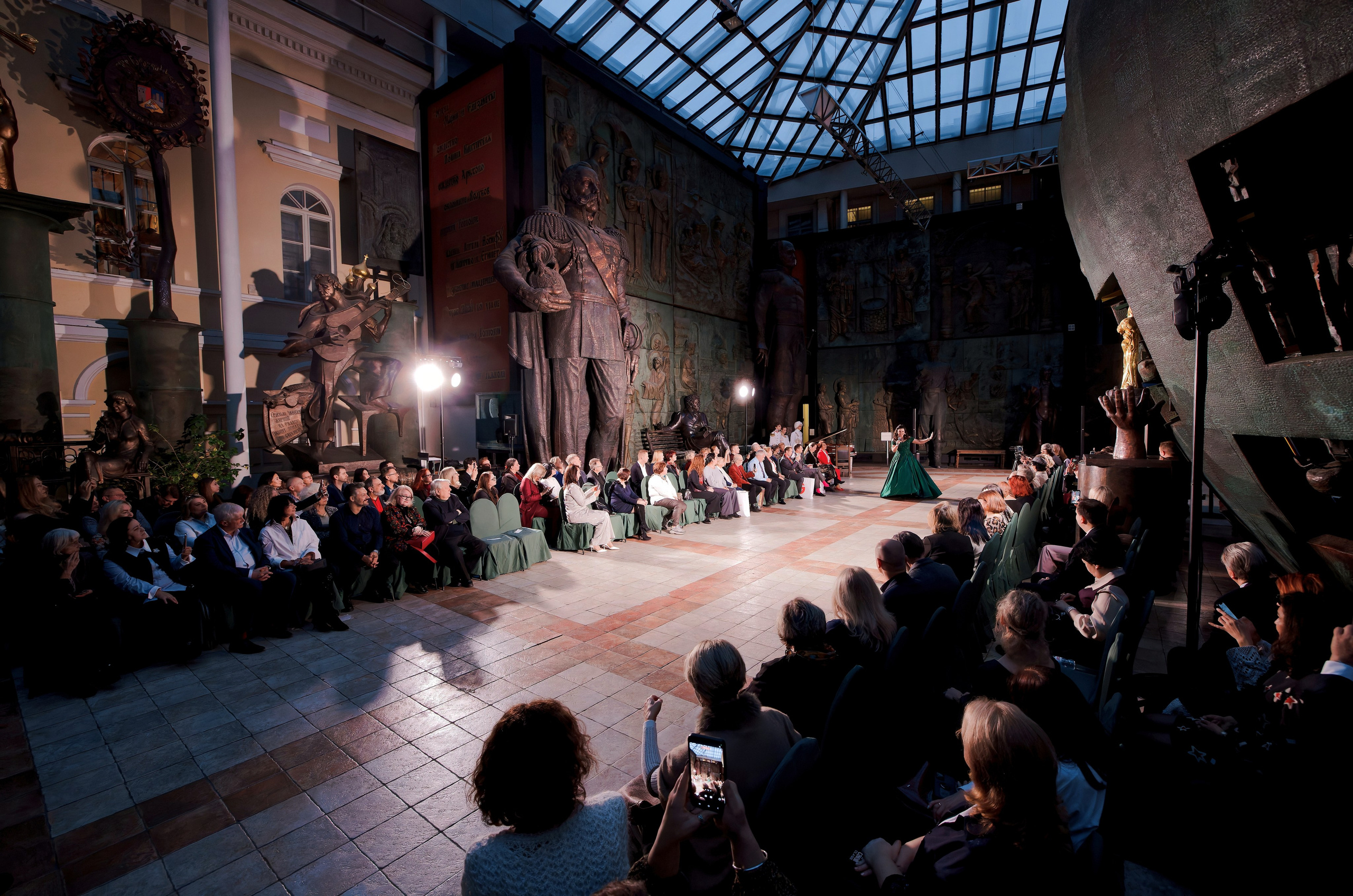 Концертное мероприятие в музее с скульптурами и барельефами - зрители слушают выступление певицы, фотосъемка культурных событий