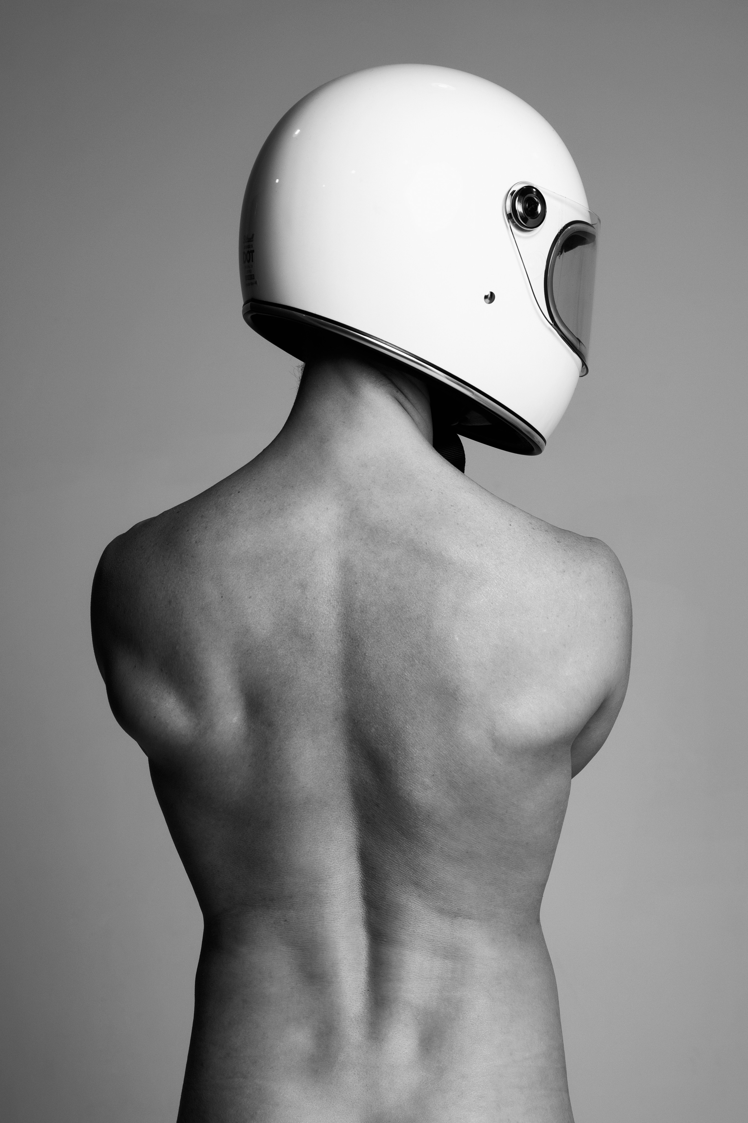 Мужская ню фотосессия в студии, мужчина в мото шлеме стоит спиной на против окна 