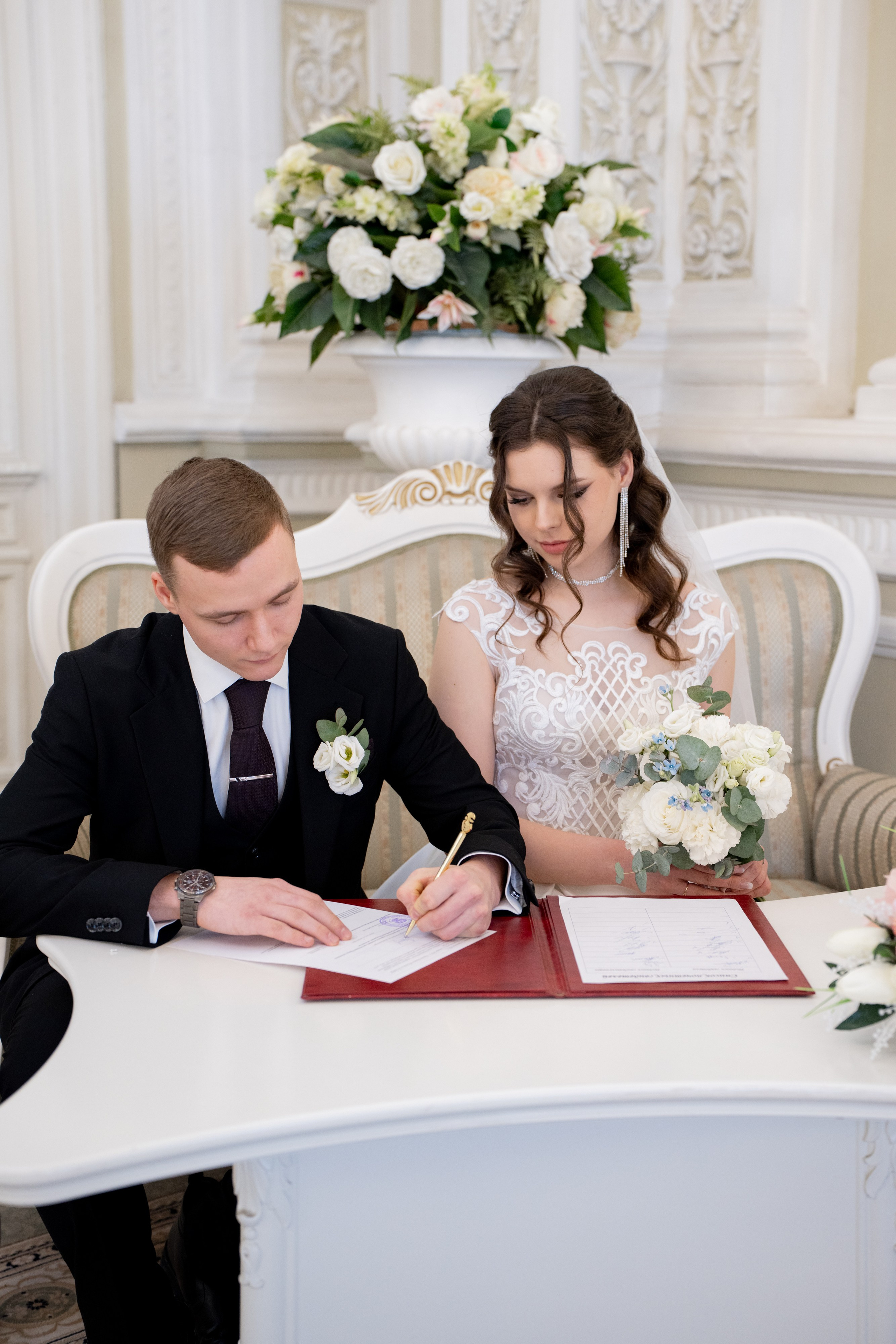 Свадебная фотосессия в Санкт-Петербурге во дворце  бракосочетания №1 на Английской набережной. Невеста и жених сидят на диване и ставят подписи в главном зале загса на регистрации.