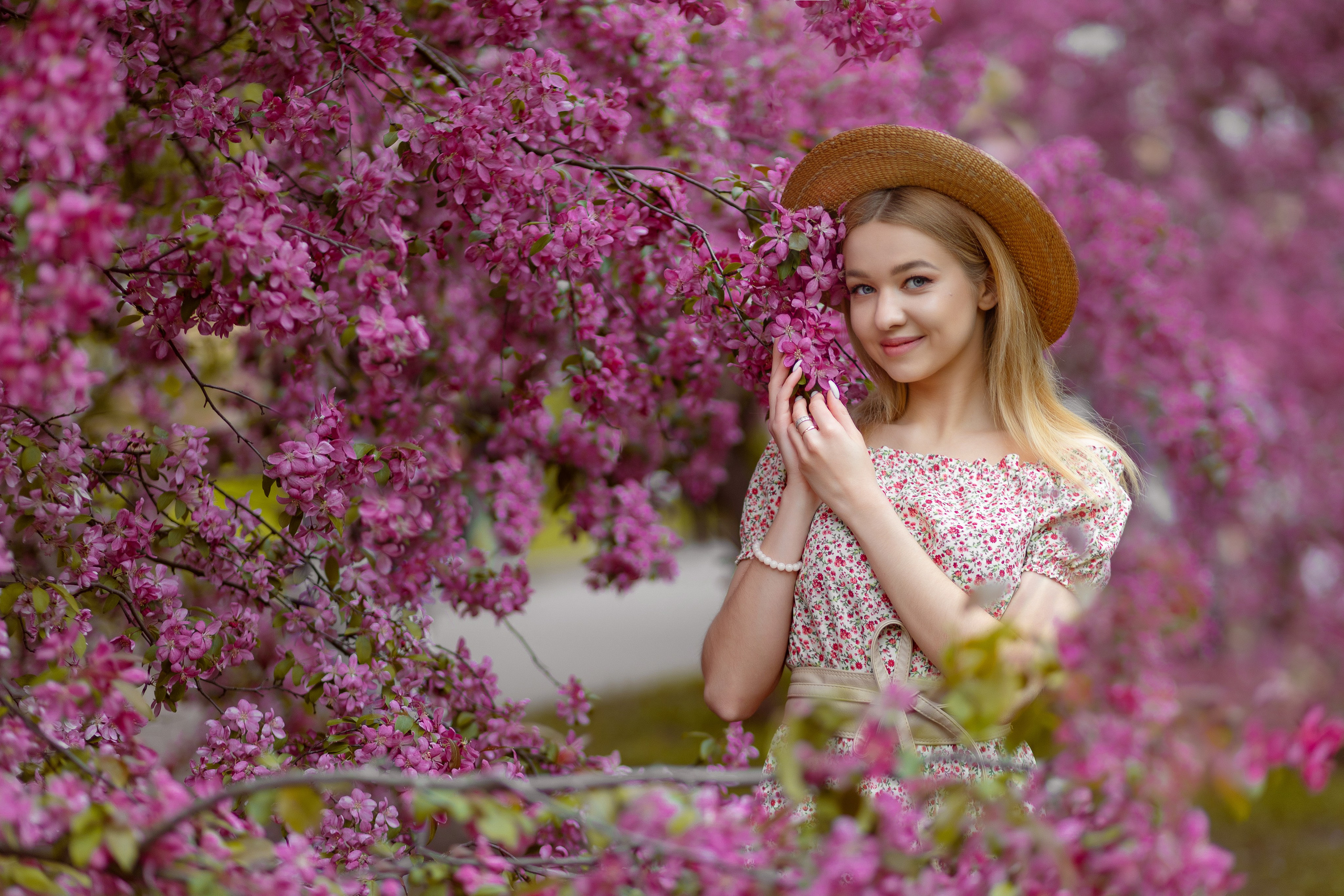 Девушка в розовом платье и соломенной шляпе окруженная ветвями цветущей яблони