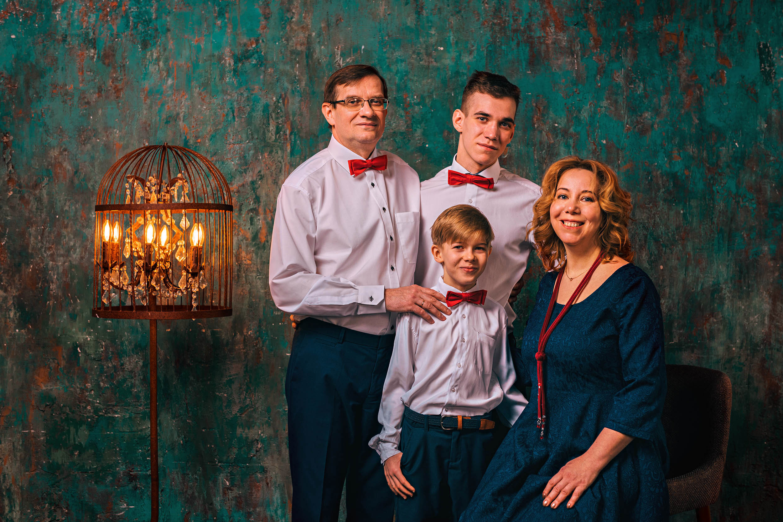 Семейный портрет в белых рубашках с красными бабочками на фоне зеленой стены и лампы, мама в синем платье