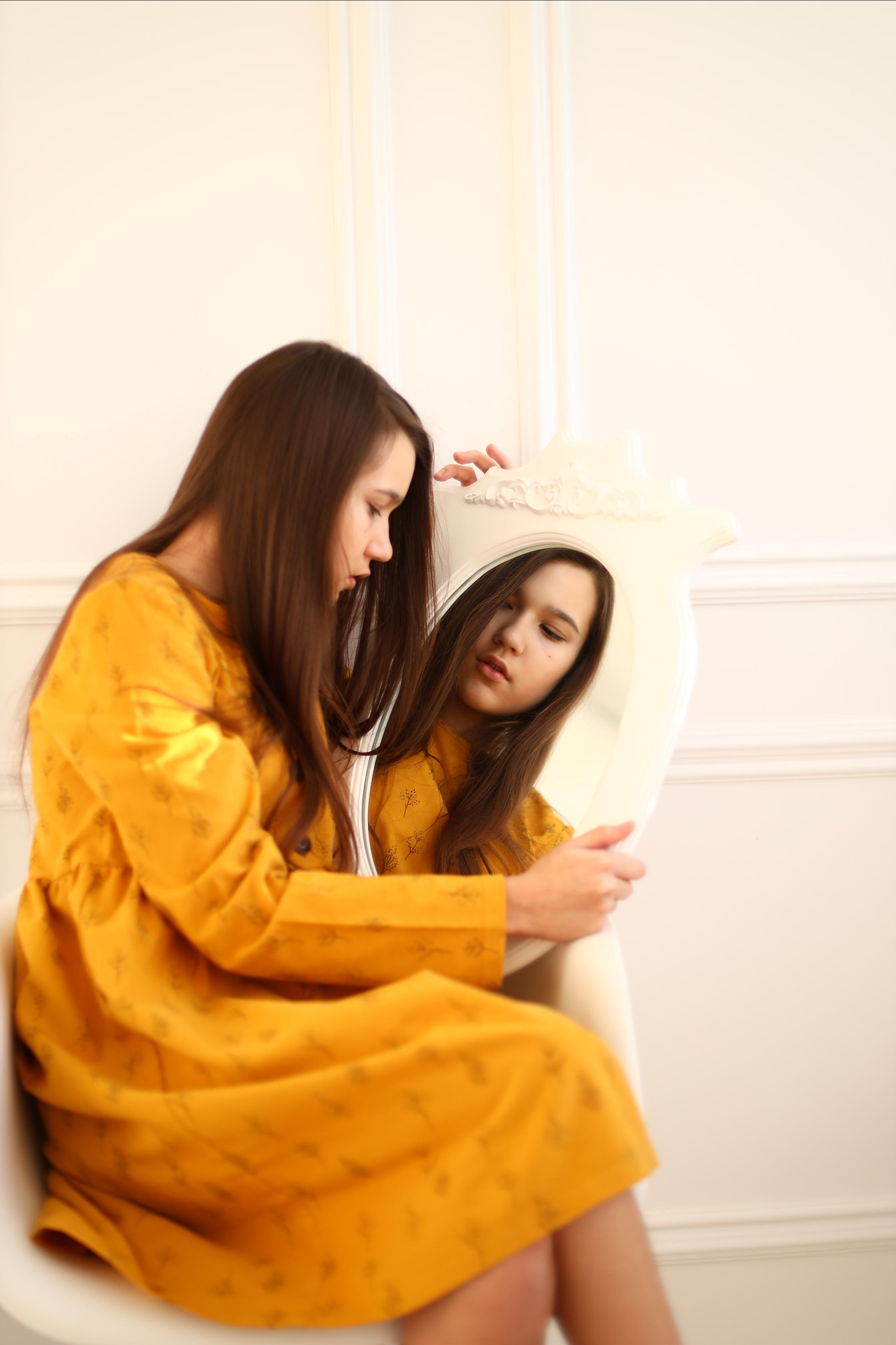 Девушка в жёлтом платье смотрит в зеркало