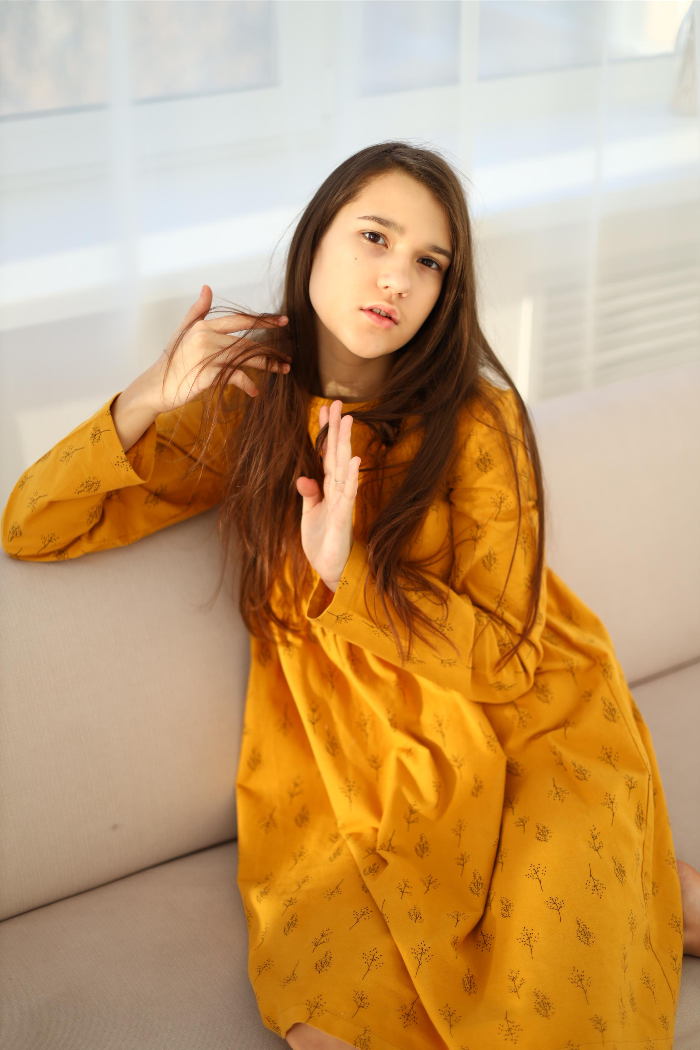 Девушка в жёлтом платье сидит на диване 