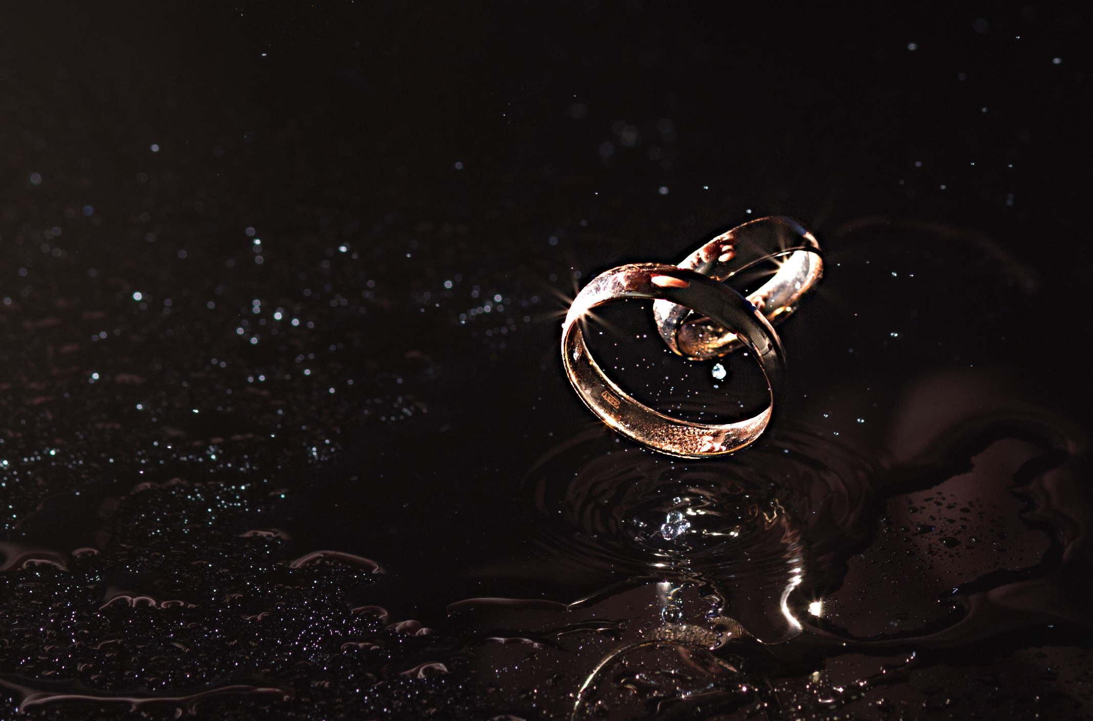 свадебные кольца парят в воздухе на темном фоне, отражаясь от зеркальной поверхности