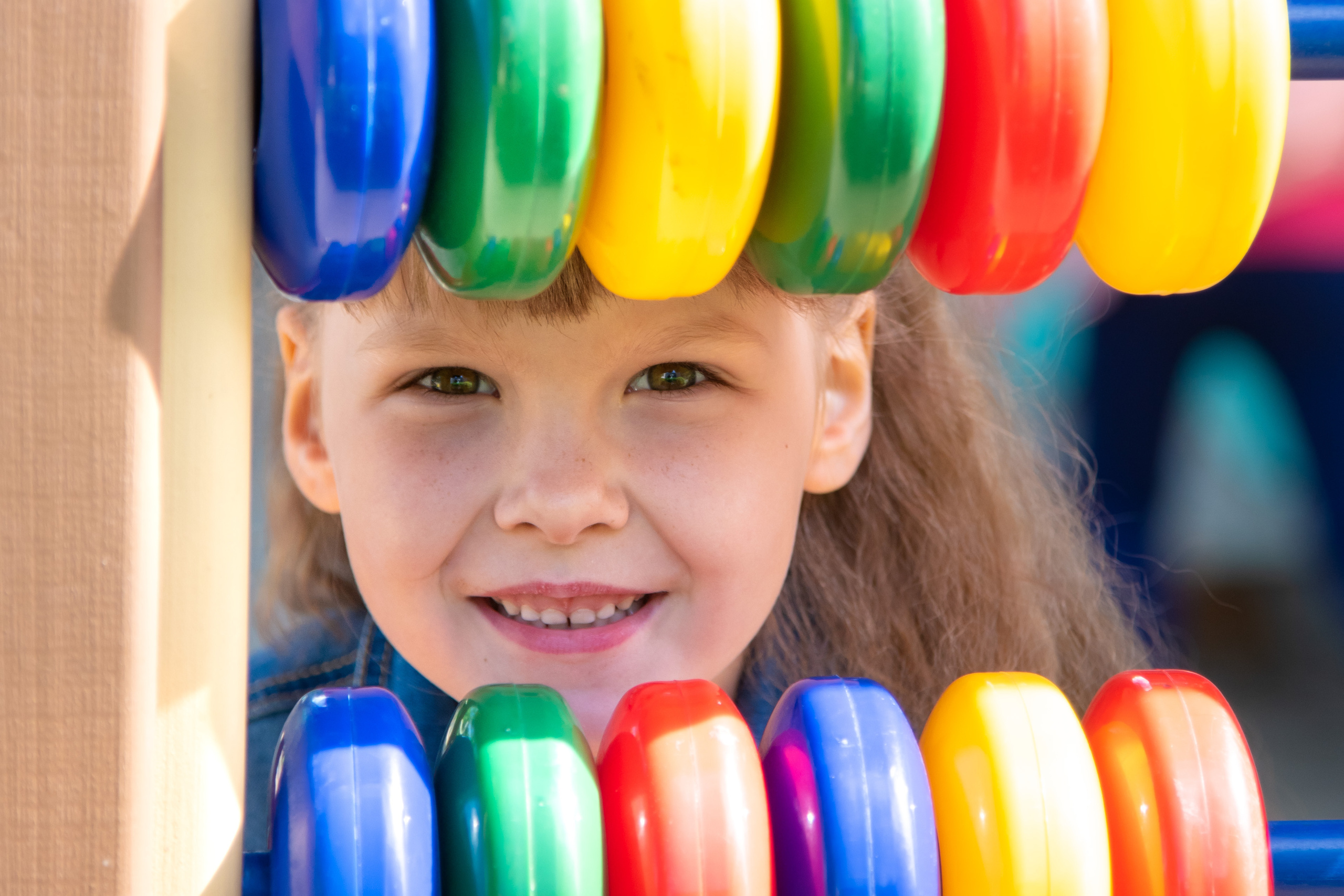 девочка спряталась за игрушкой в детском саду. Яркий кадр сделан в солнечную погоду