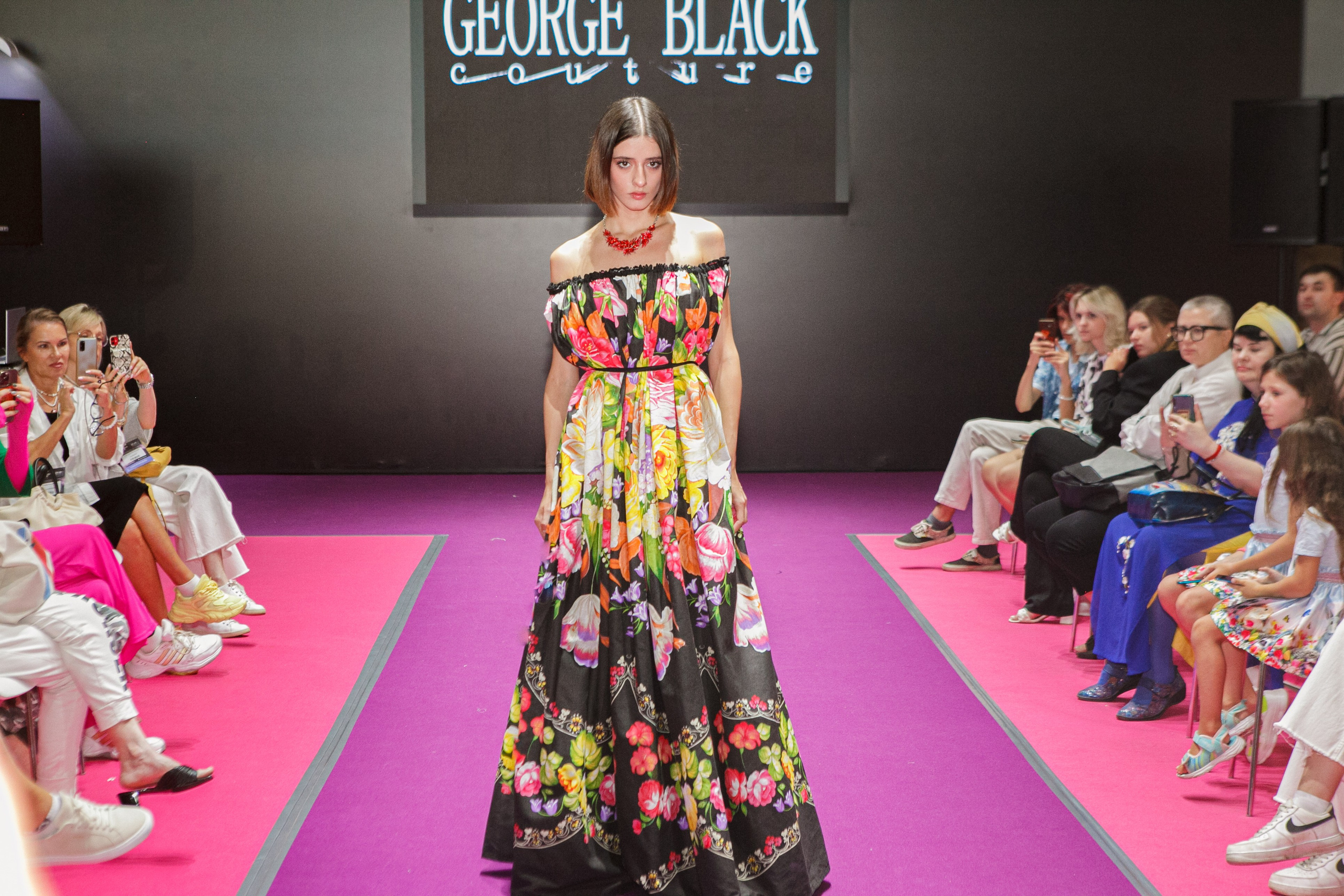  "Модели в ярких нарядах проходят по подиуму во время показа мод, освещенные яркими софитами и окруженные восторженными зрителями."