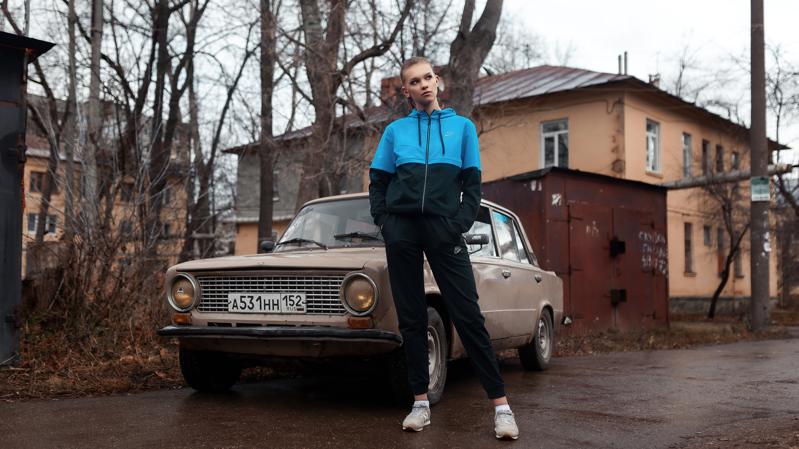 Портретный фотограф в Нижнем Новгороде. Необычные фотосессии в Нижнем Новгороде. Заказать фотосессию. Девушка красивый гопник в синем спортивном костюме на фоне бежевой спортивной лада жигули машины и старого города осенью.