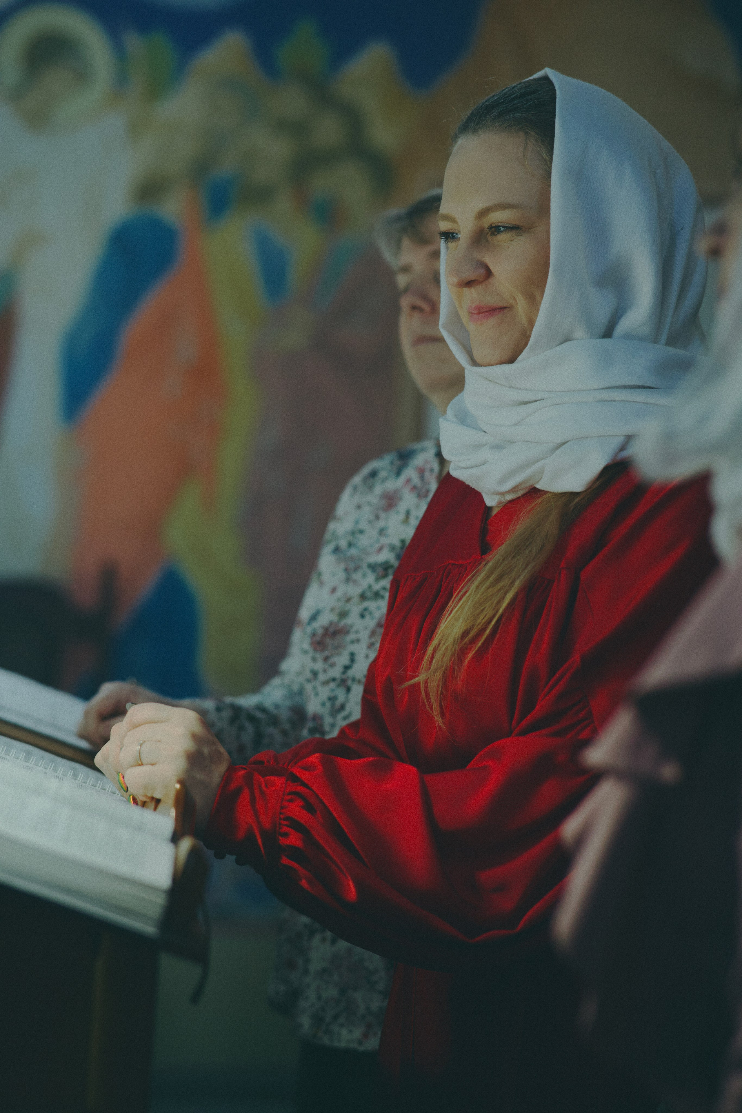 Женщина в красной блузе и белом платке сосредоточенно читает с аналоя в храме. Традиционный образ православной прихожанки