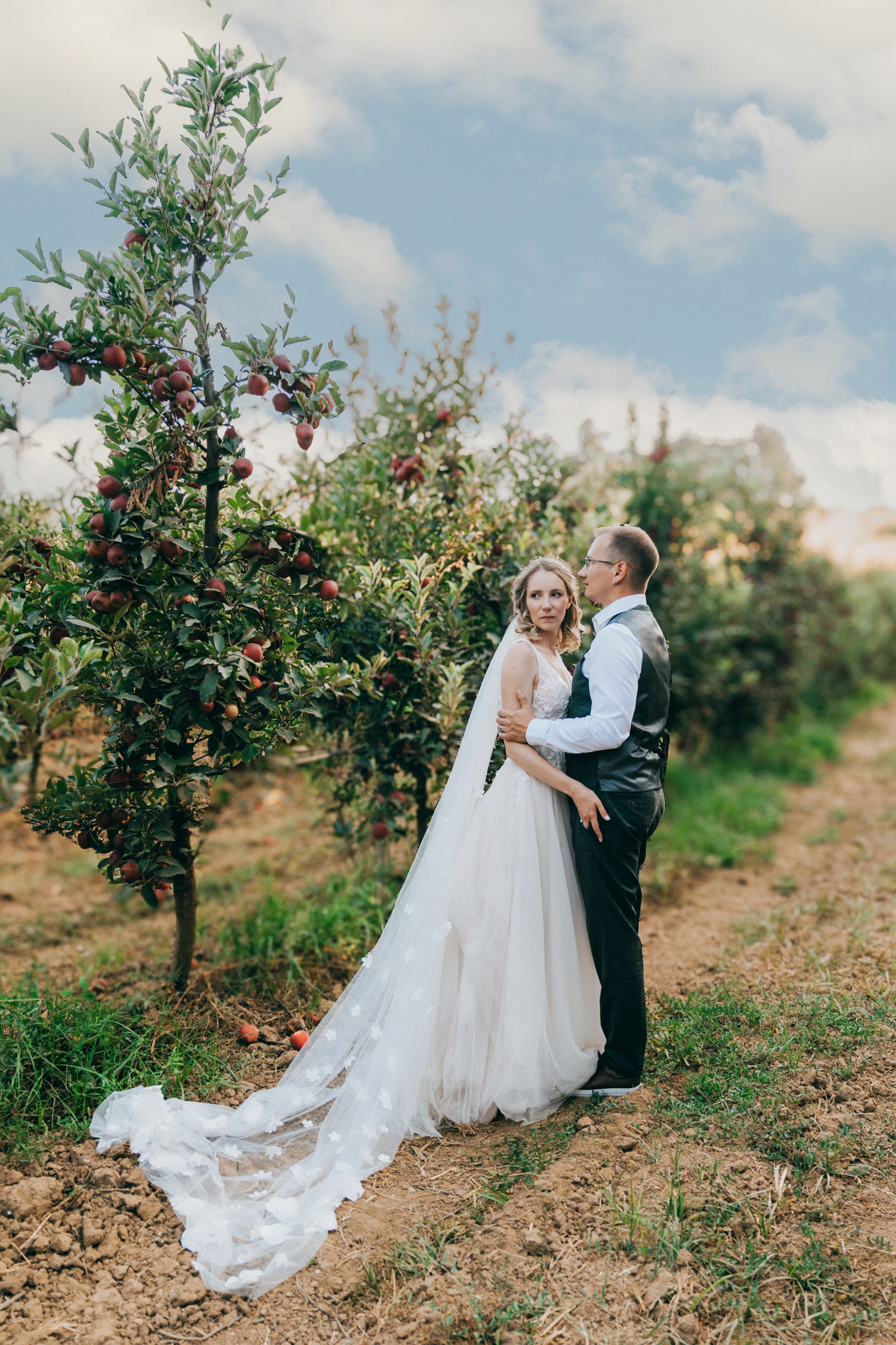 Жених и невеста обнимаются среди яблоневого сада, вокруг созревшие яблоки.