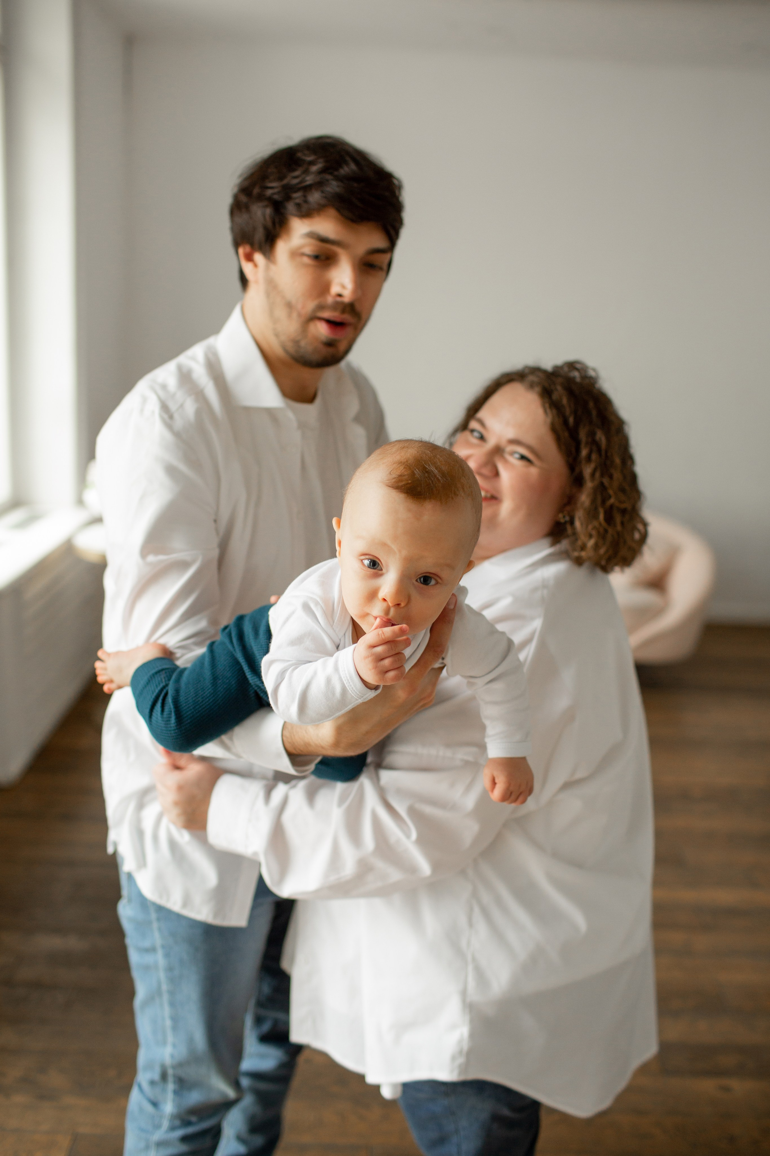 Живая семейная фотография: малыш смеется на руках у родителей.