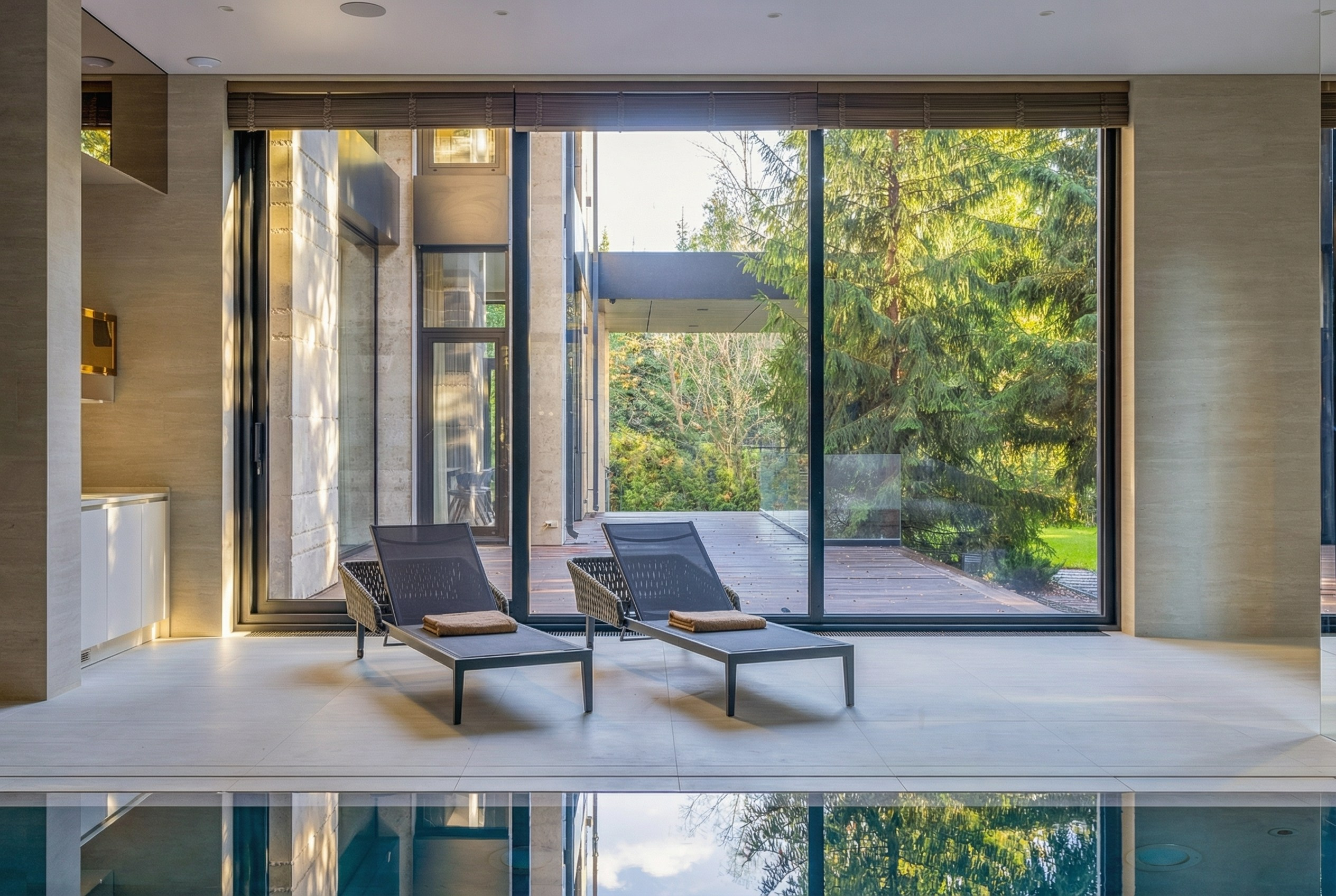 Зона отдыха у 12-метрового бассейна с панорамным остеклением и видом на лес, шезлонги на фоне террасы, проект Валерии Котович в Подмосковье.