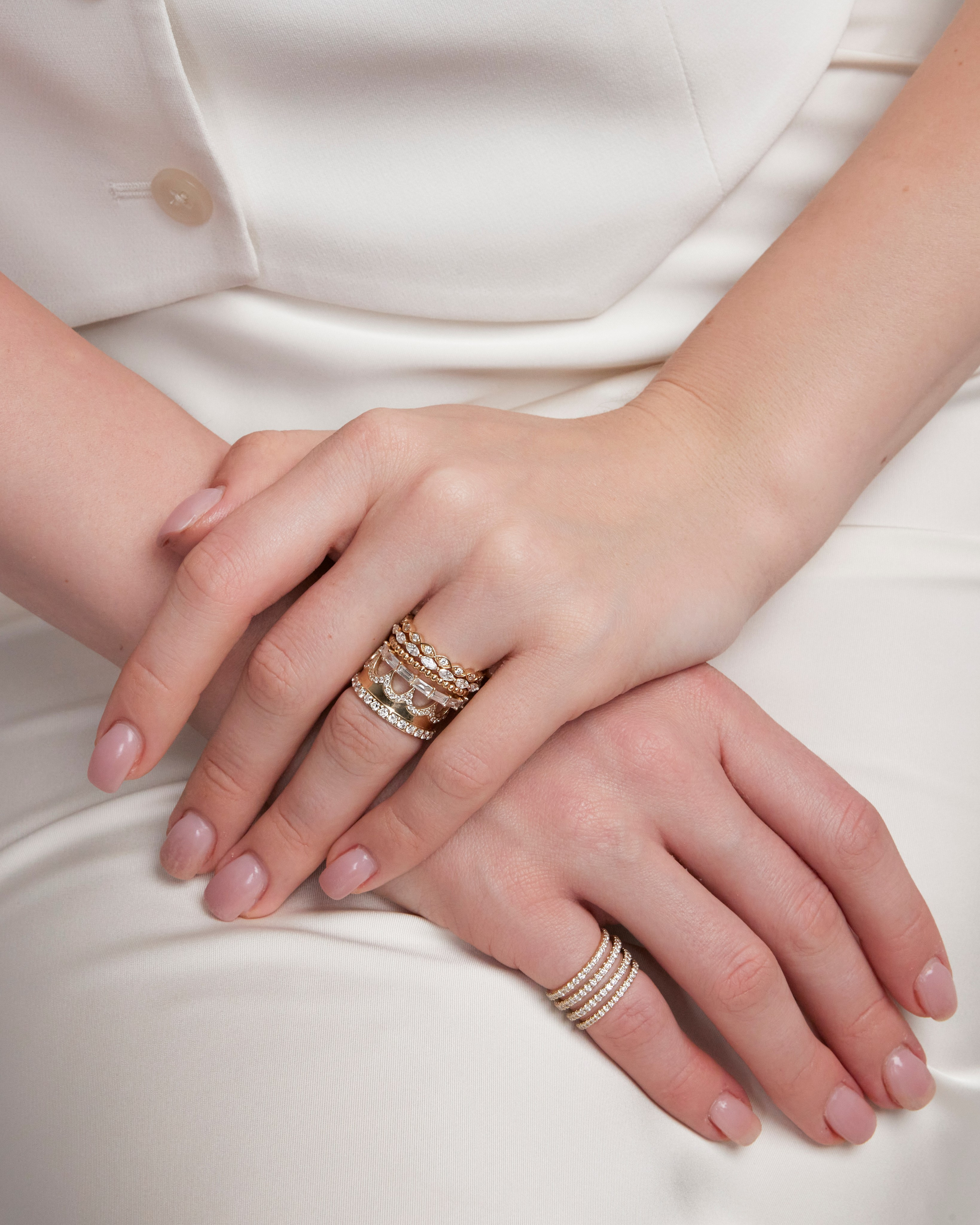 Manicured hands adorned with layered gold rings, showcasing modern and elegant accessories.