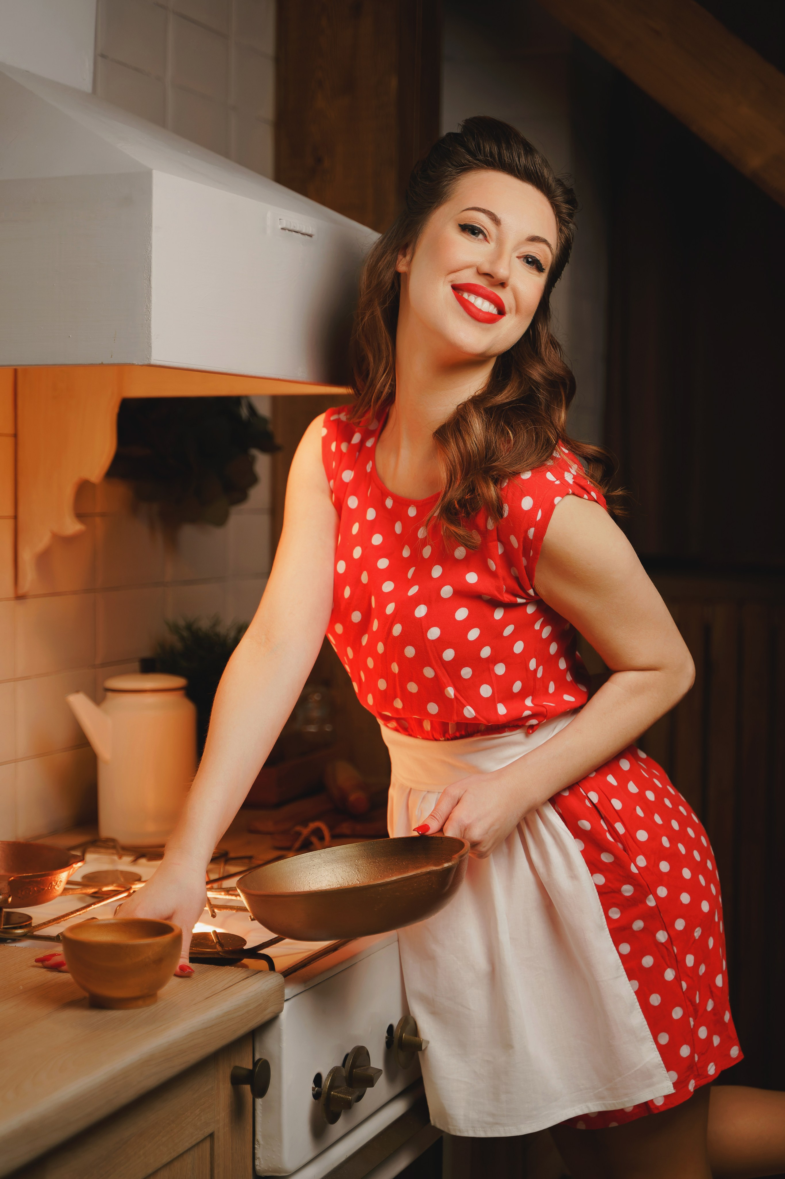 Девушка на кухне. Держит в руках сковороду и улыбается.