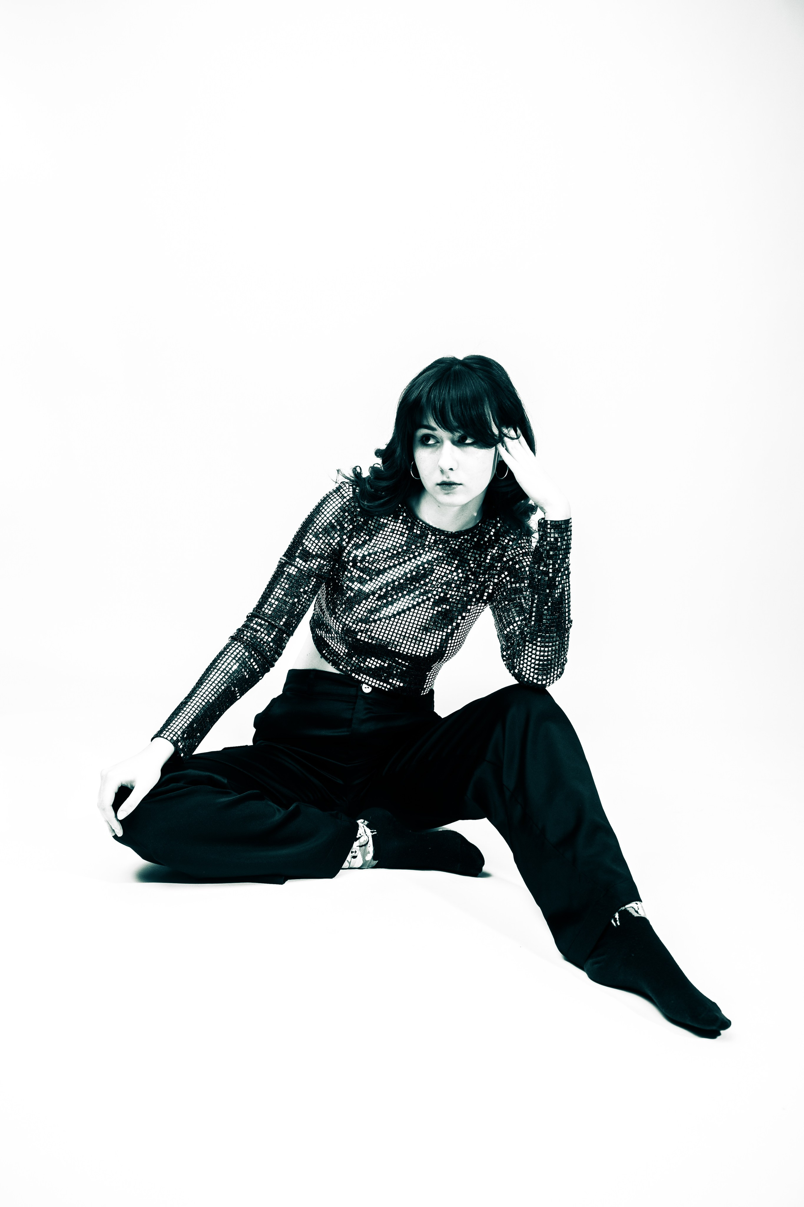 Девушка в черном топе и широких брюках позирует с веером.