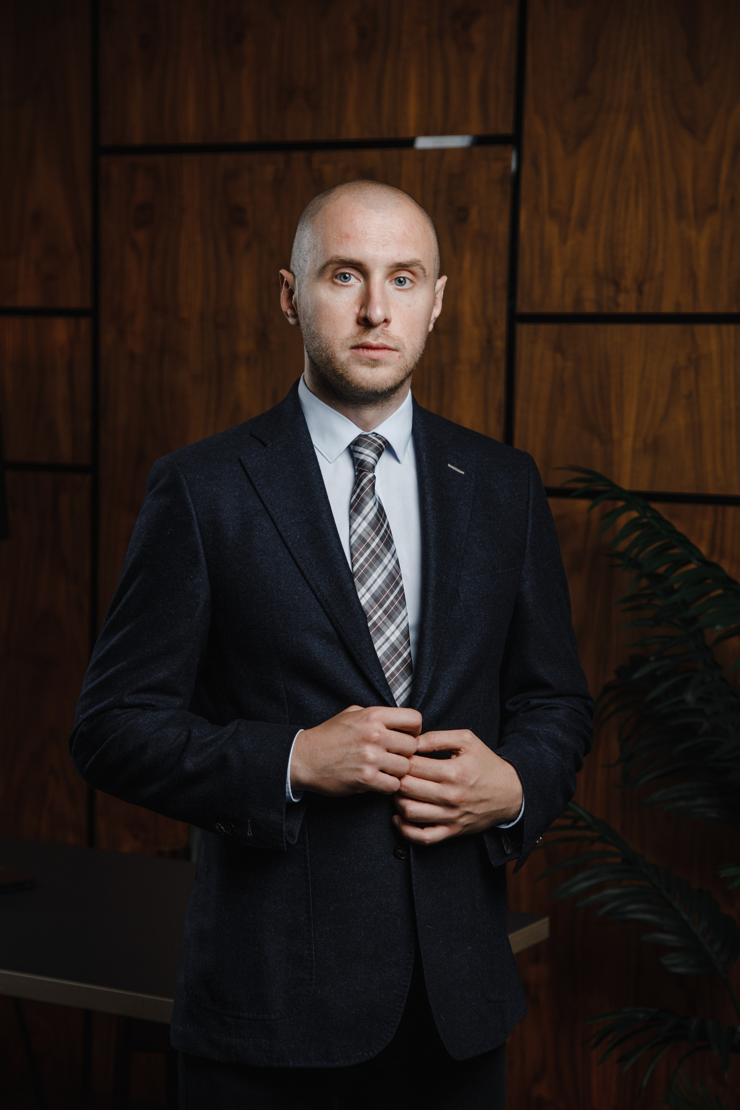 Мужчина в темно-синем пиджаке застегивает пуговицу на фоне деревянной стены в офисе, фотограф Жуков Василий из Москвы