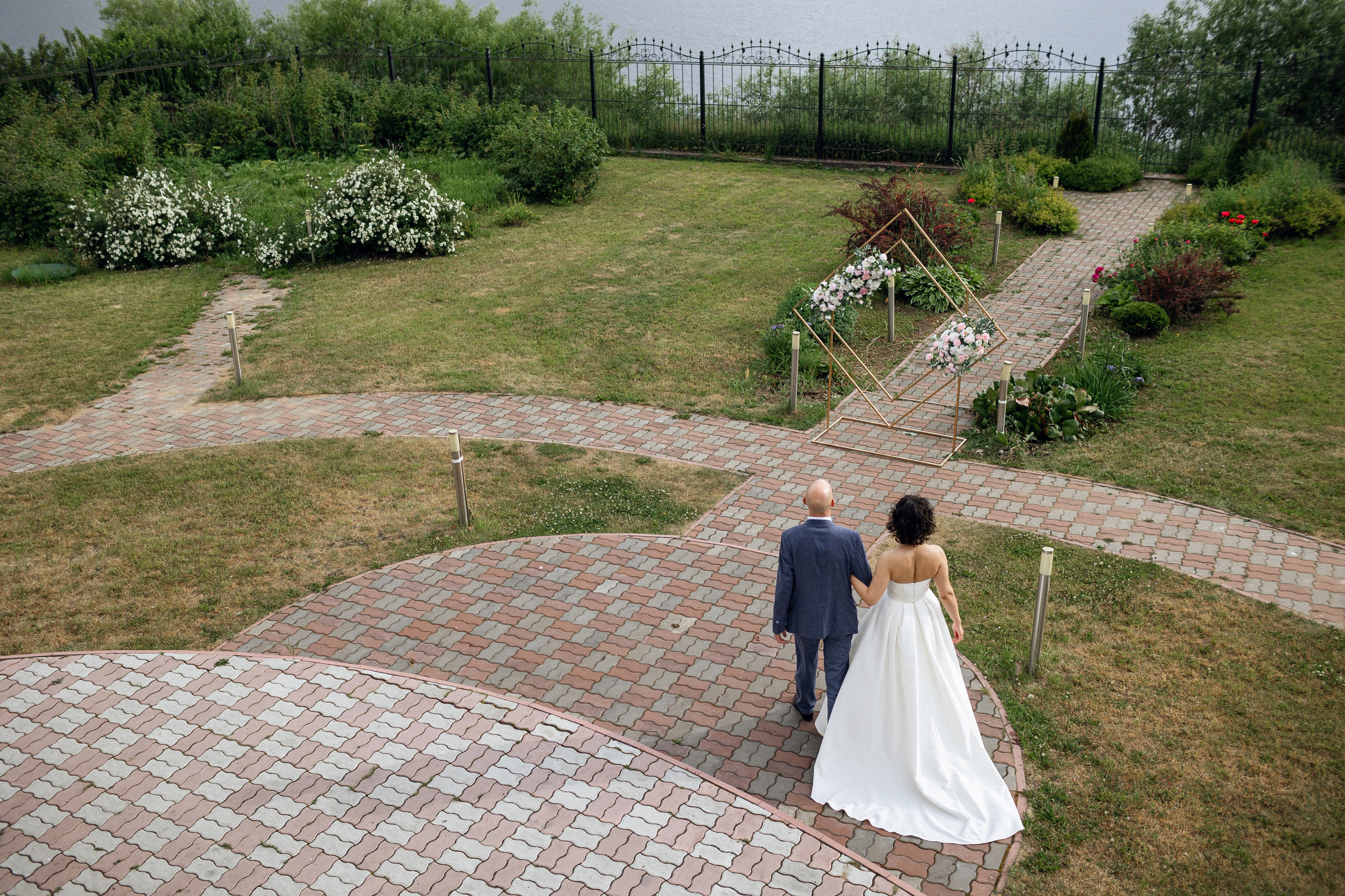 Вид с балкона красивого особняка в Архангельске: жених и невеста гуляют по каменной дорожке среди цветущих клумб — работа фотографа Клещинова Алексея