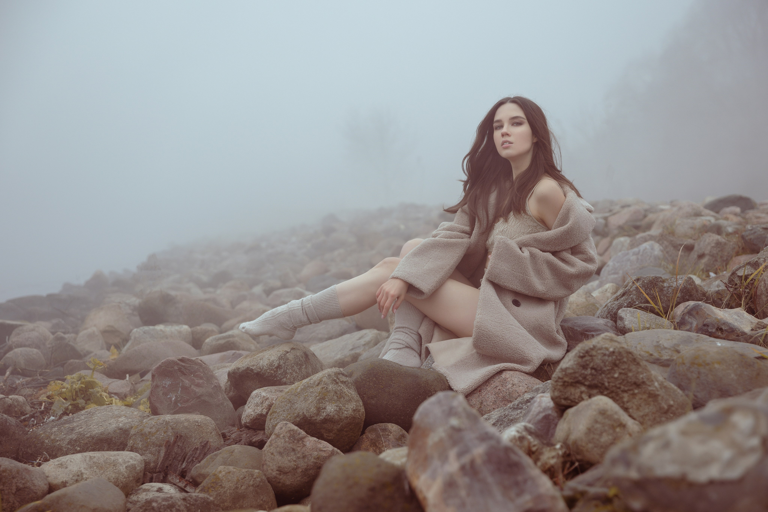 Девушка сидит на больших валунах в туманном парке Коломенское