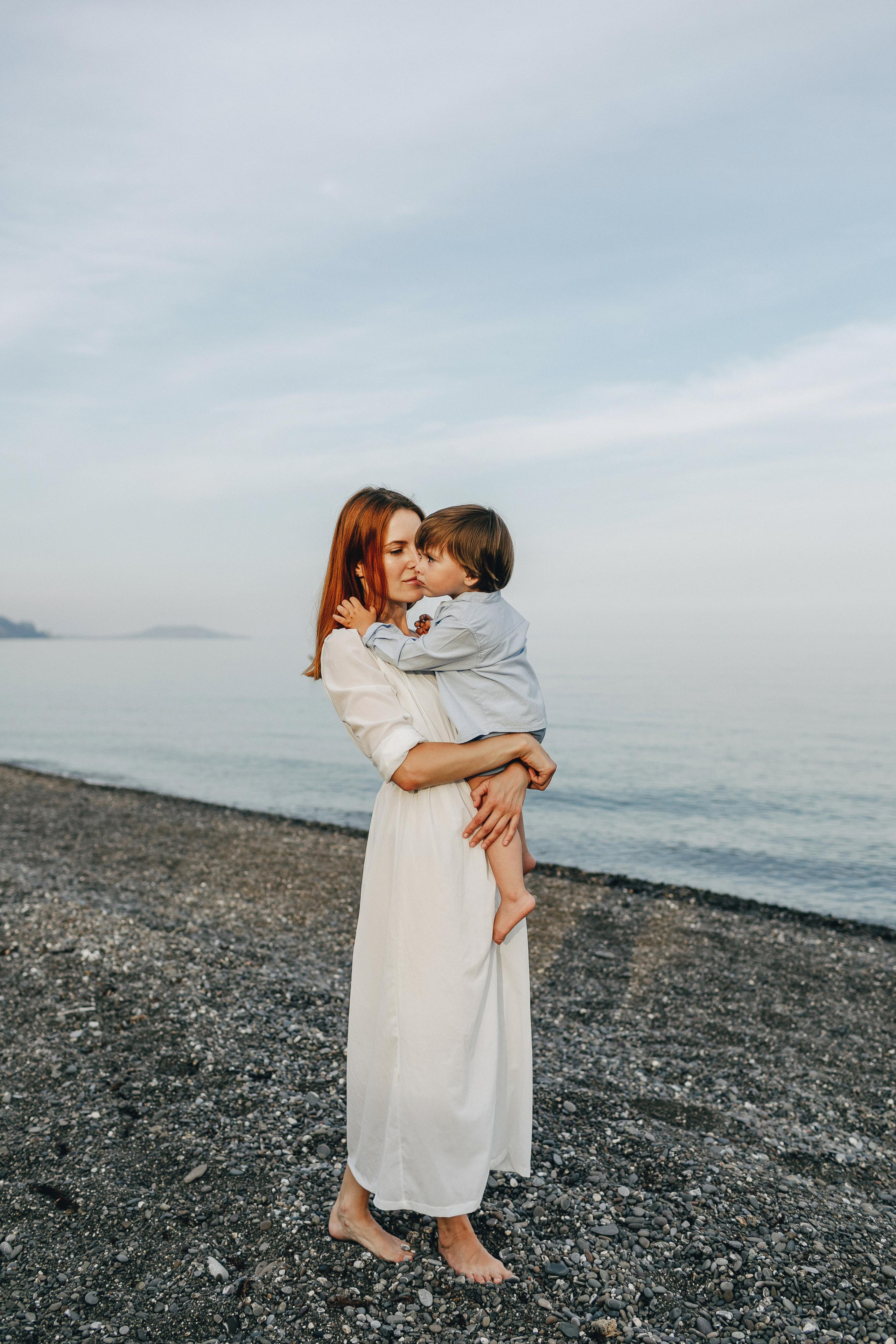 Мама обнимает своего ребенка, стоя у моря.
