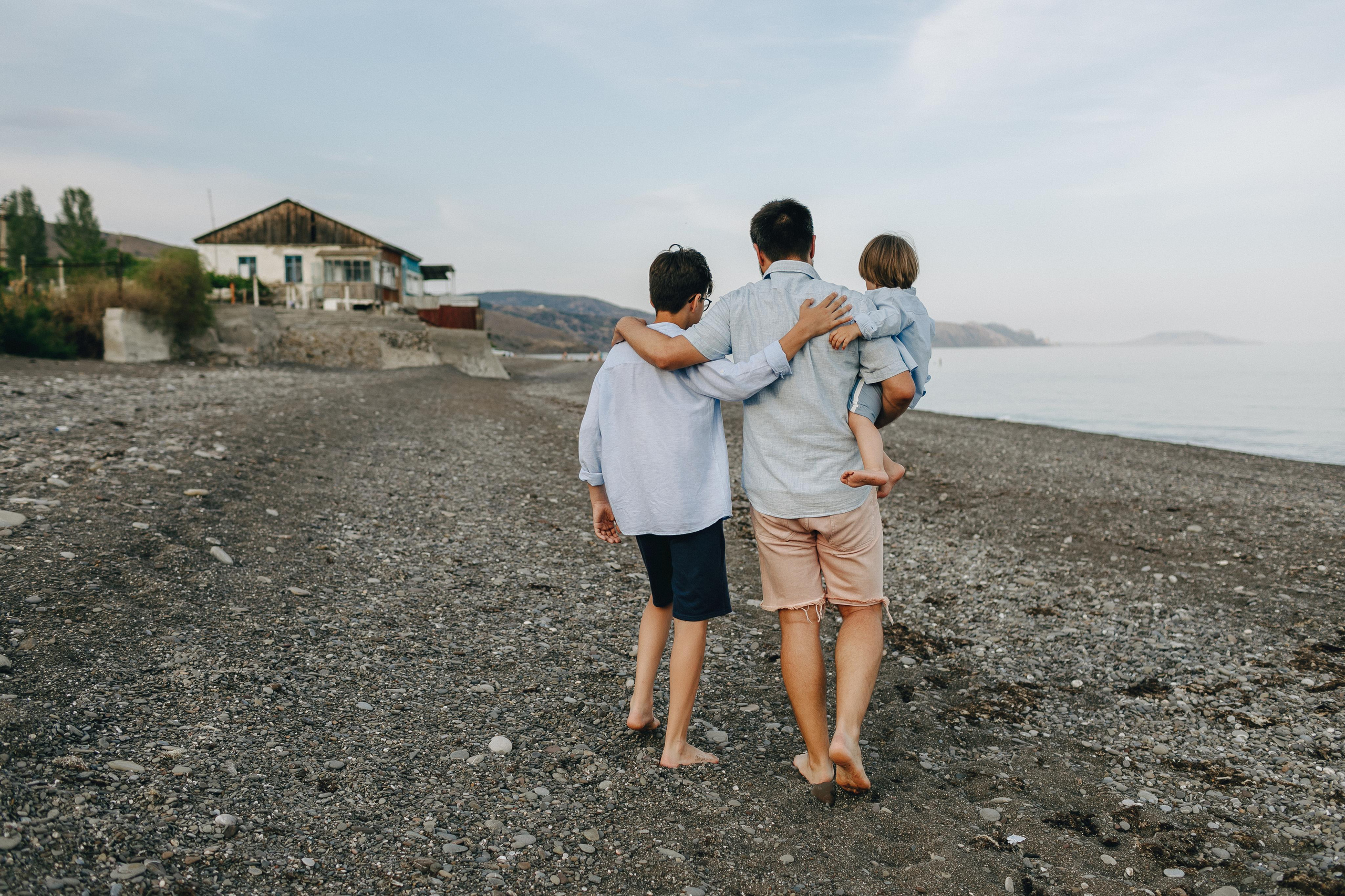 Отец обнимает своих сыновей, прогуливаясь у Крымского моря.