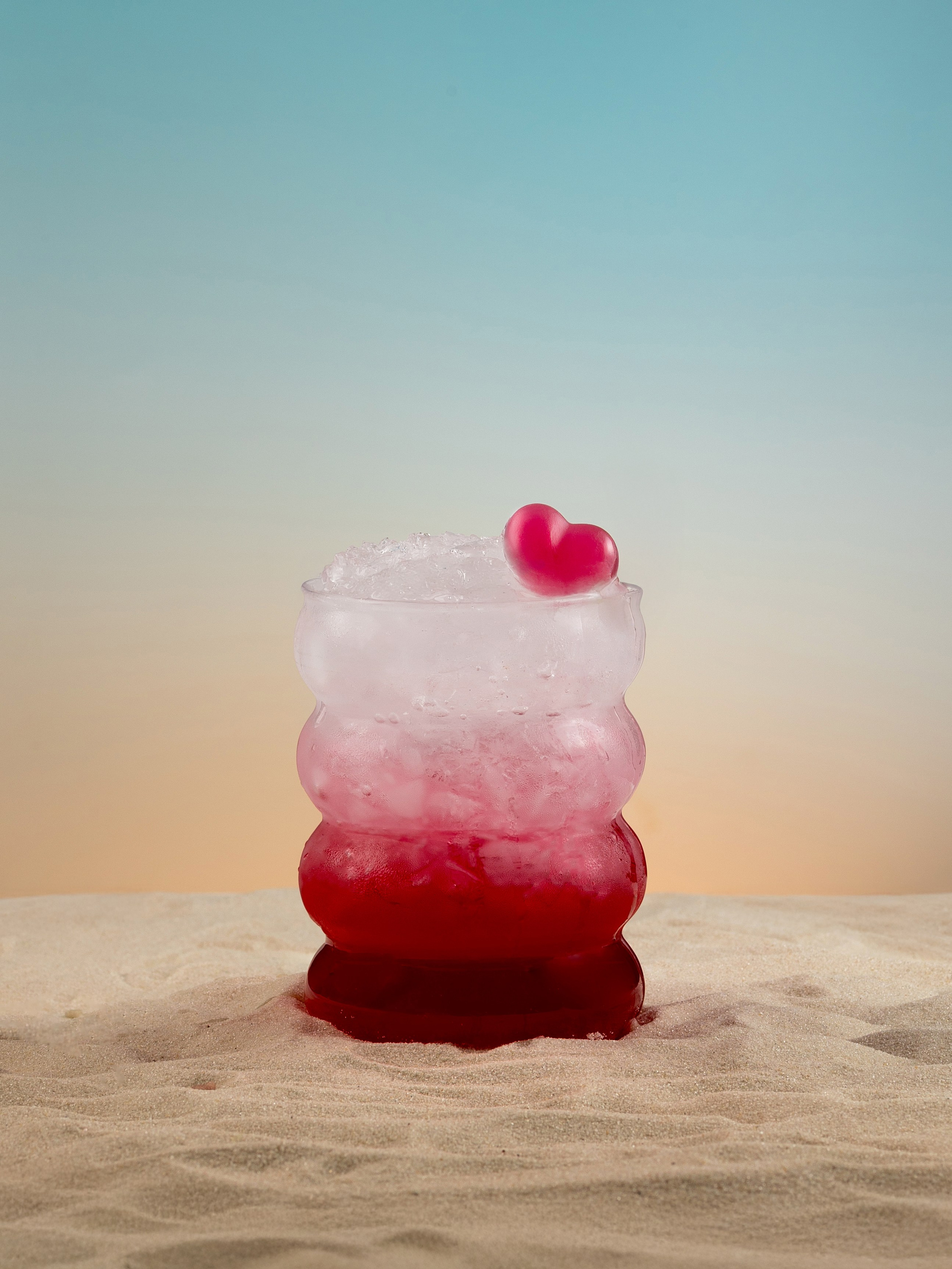 Ягодный коктейль с краш-льдом на песке на фоне закатного неба.