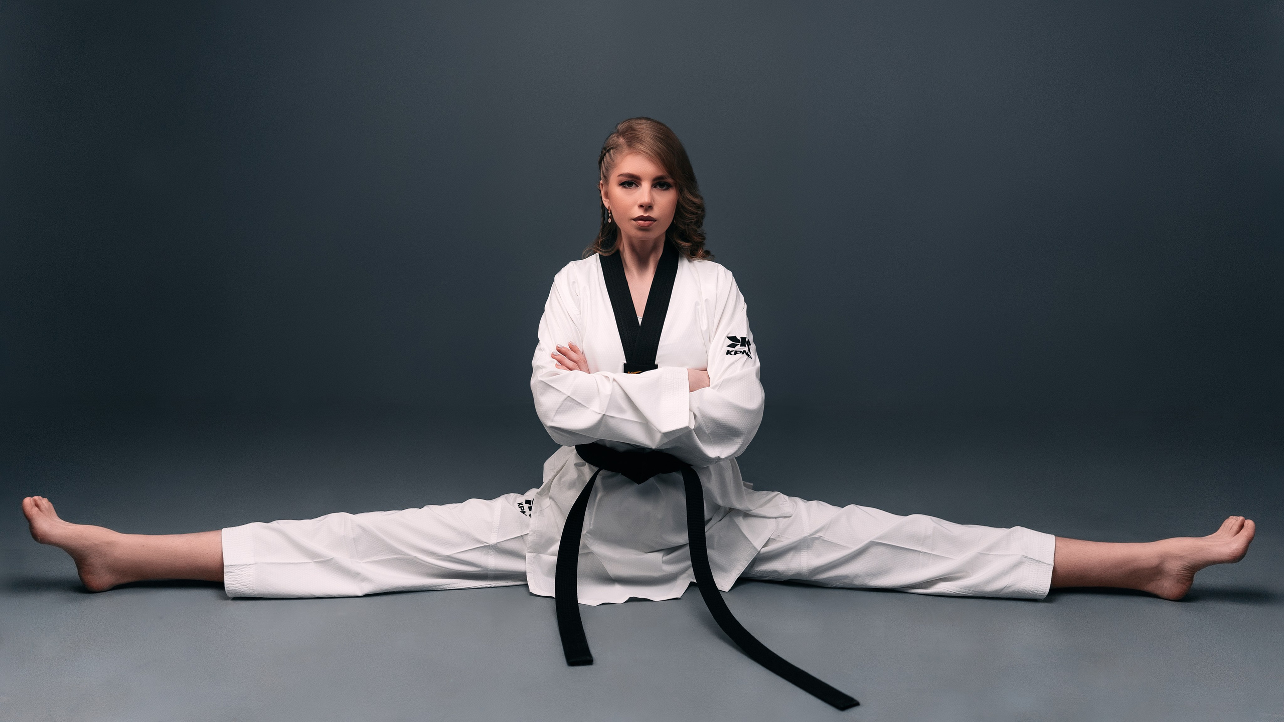 Девушка тхэквондистка, одетая в белое кимоно села на шпагат.