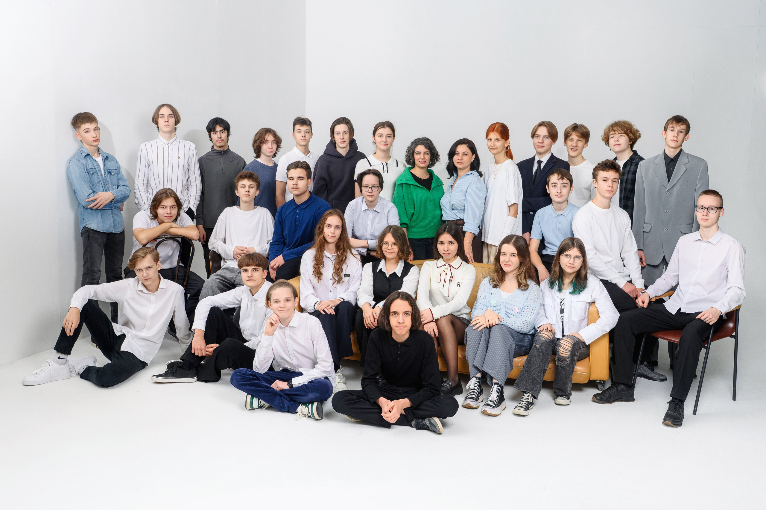 Большая группа выпускников и педагогов позирует на светлом фоне в студии.