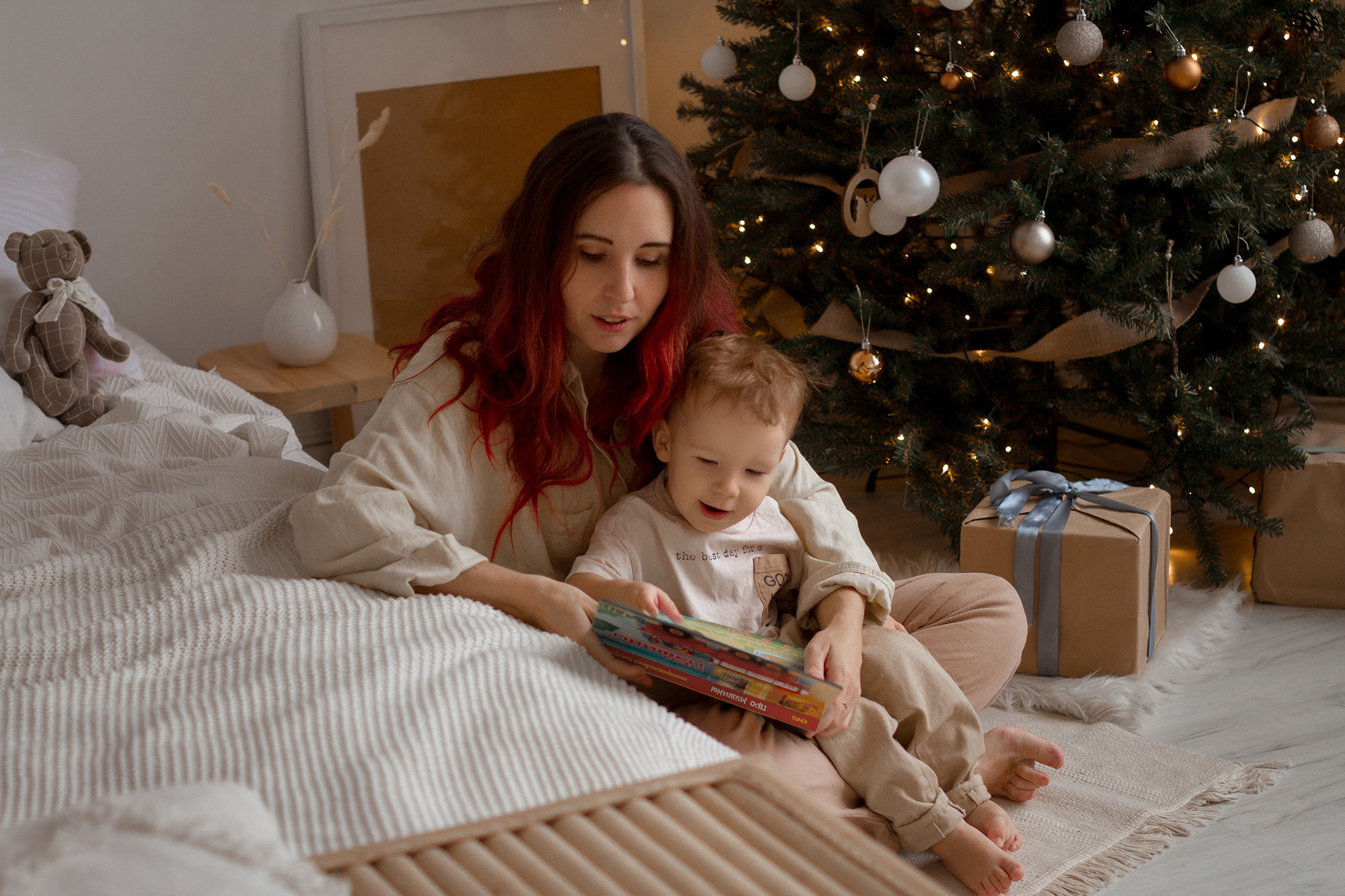 Мама и сын сидят на полу у елки и читают книгу
