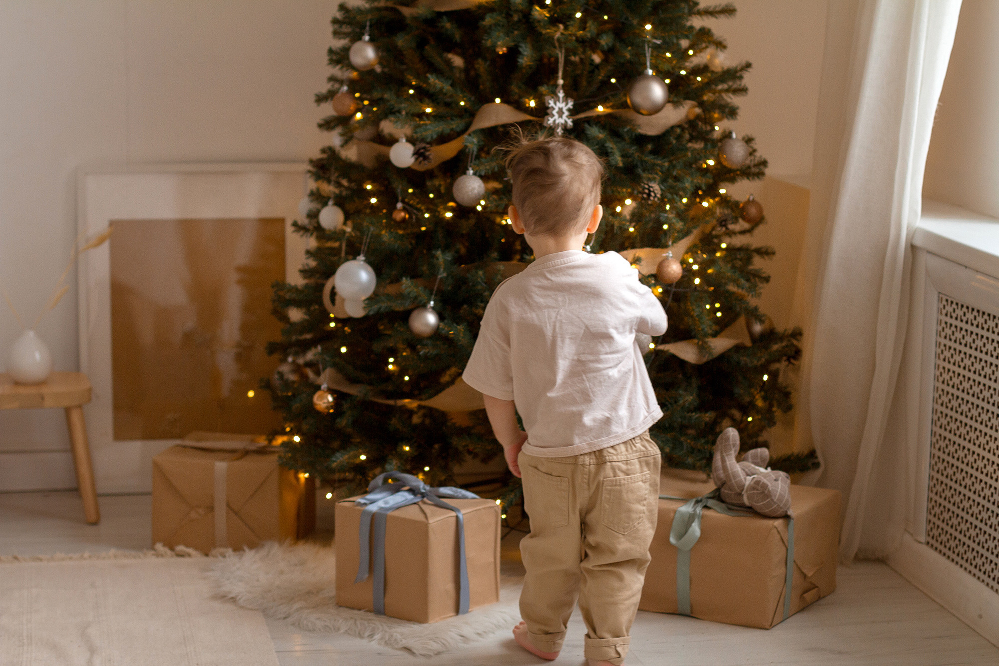 Маленький мальчик стоит рядом с новогодней елкой