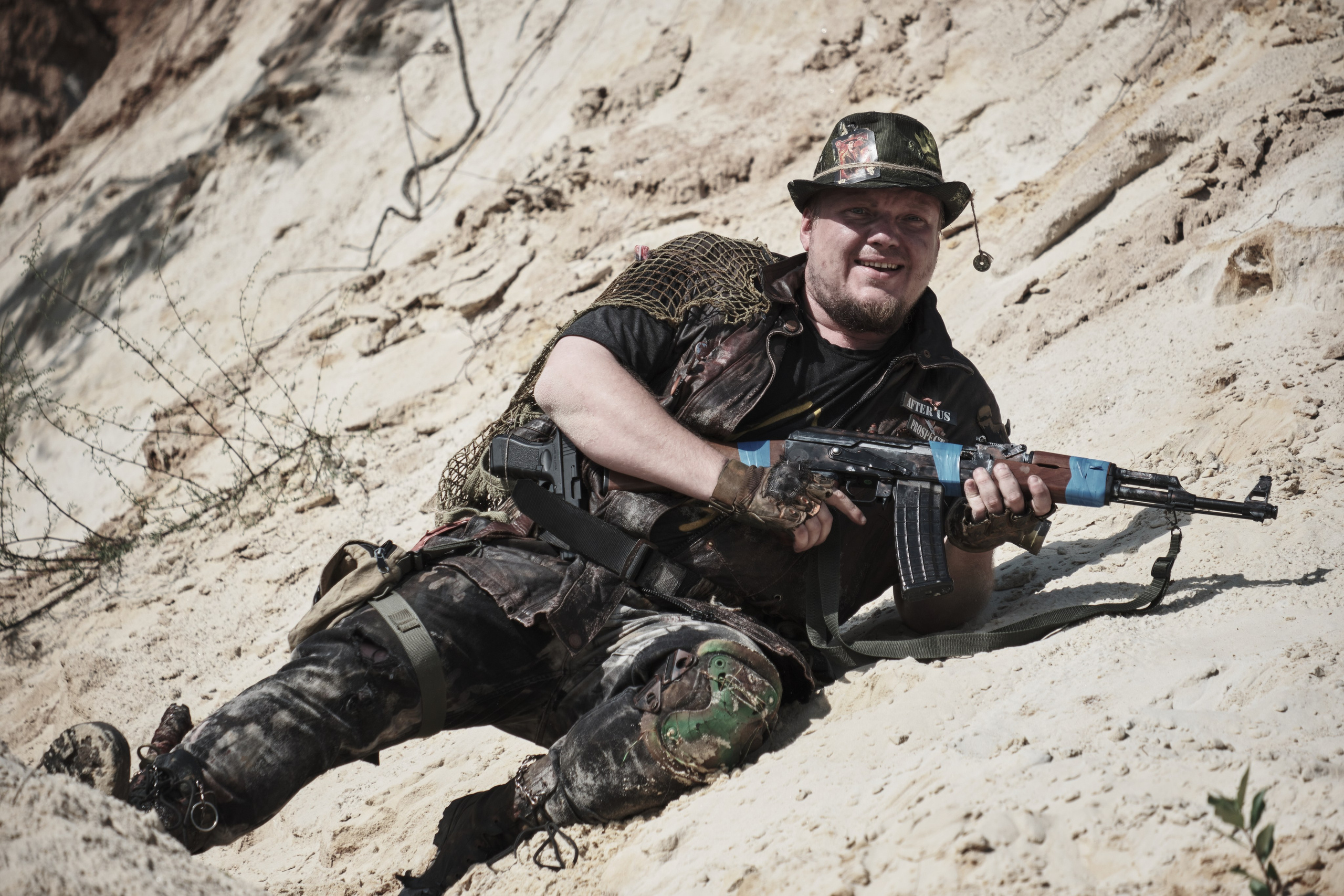 Мужчина в боевом костюме с автоматом лежит на песке
