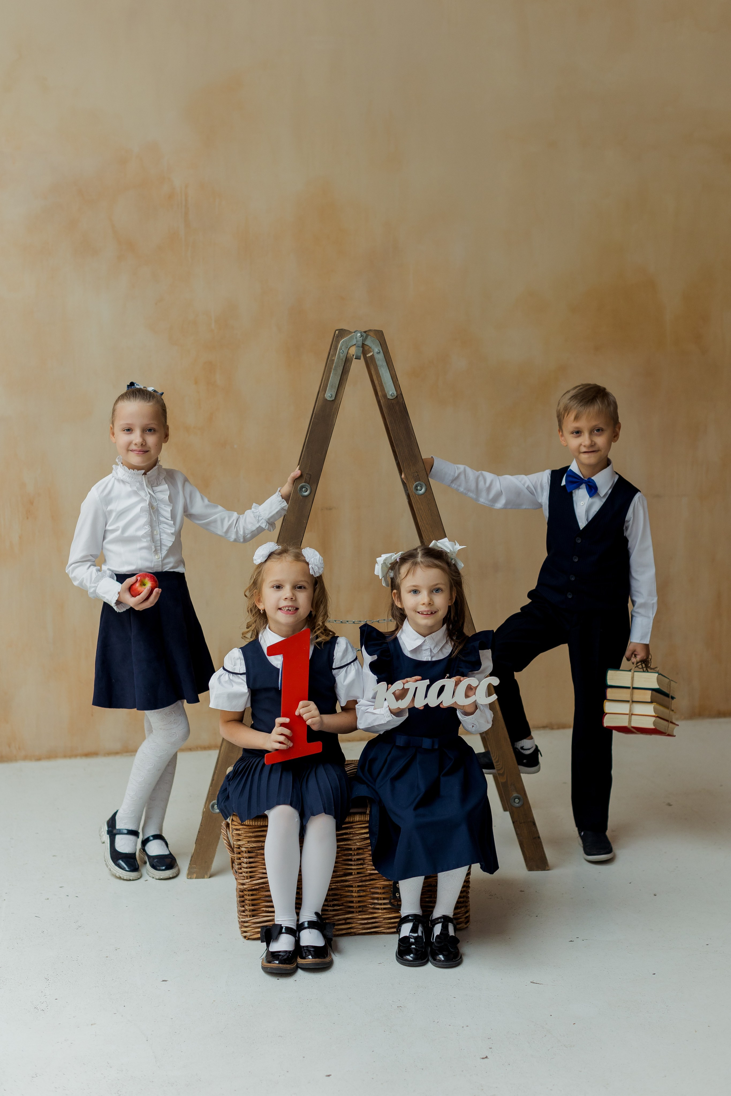 Девочки и мальчик стоят около лестницы с книгами и надписью 1 класс