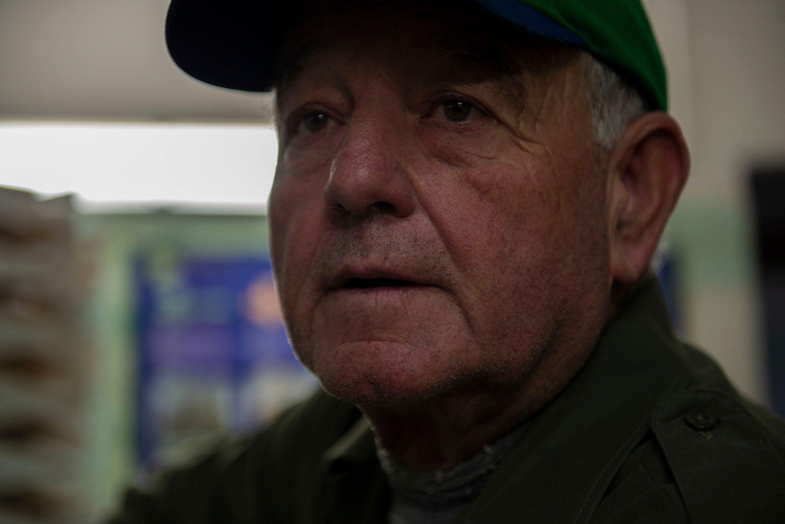 Крупный план лица пожилого итальянского фермера или владельца бизнеса, одетого в зеленую рубашку и сине-зеленую кепку.