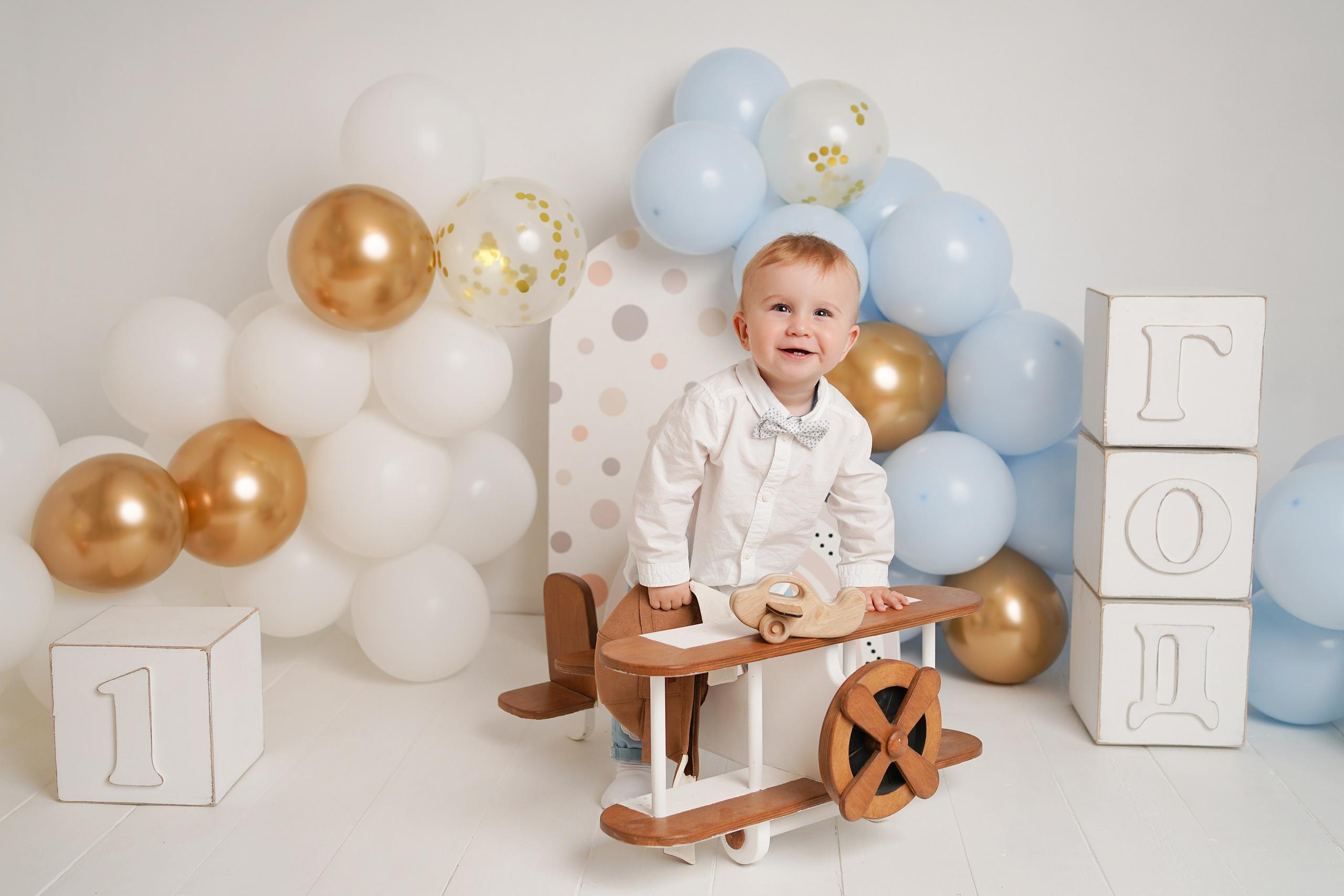 На фото изображен малыш, самолет голубые шары, кубики год.