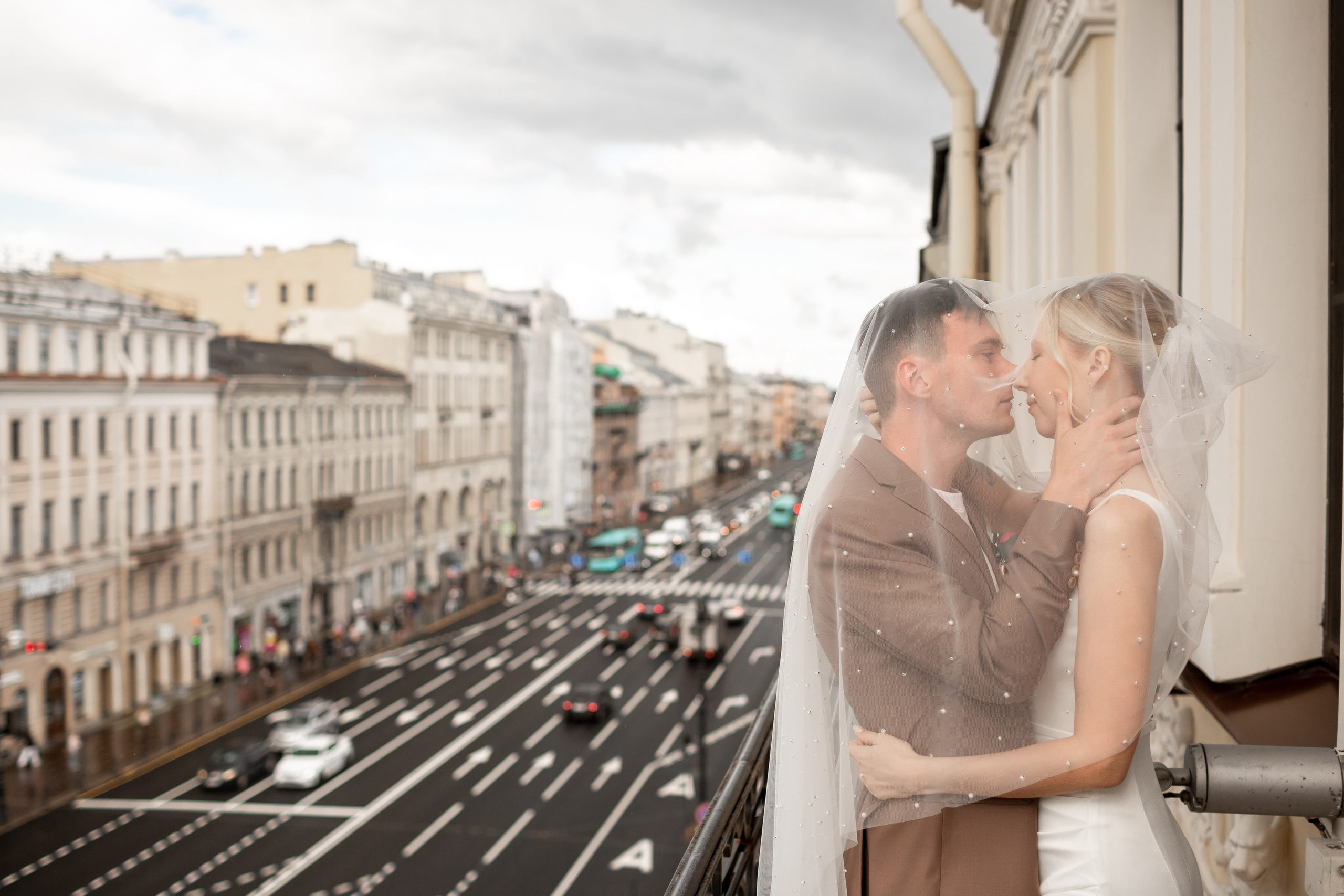 Жених целует невесту под фатой на видовом балконе в отеле Петербурга.