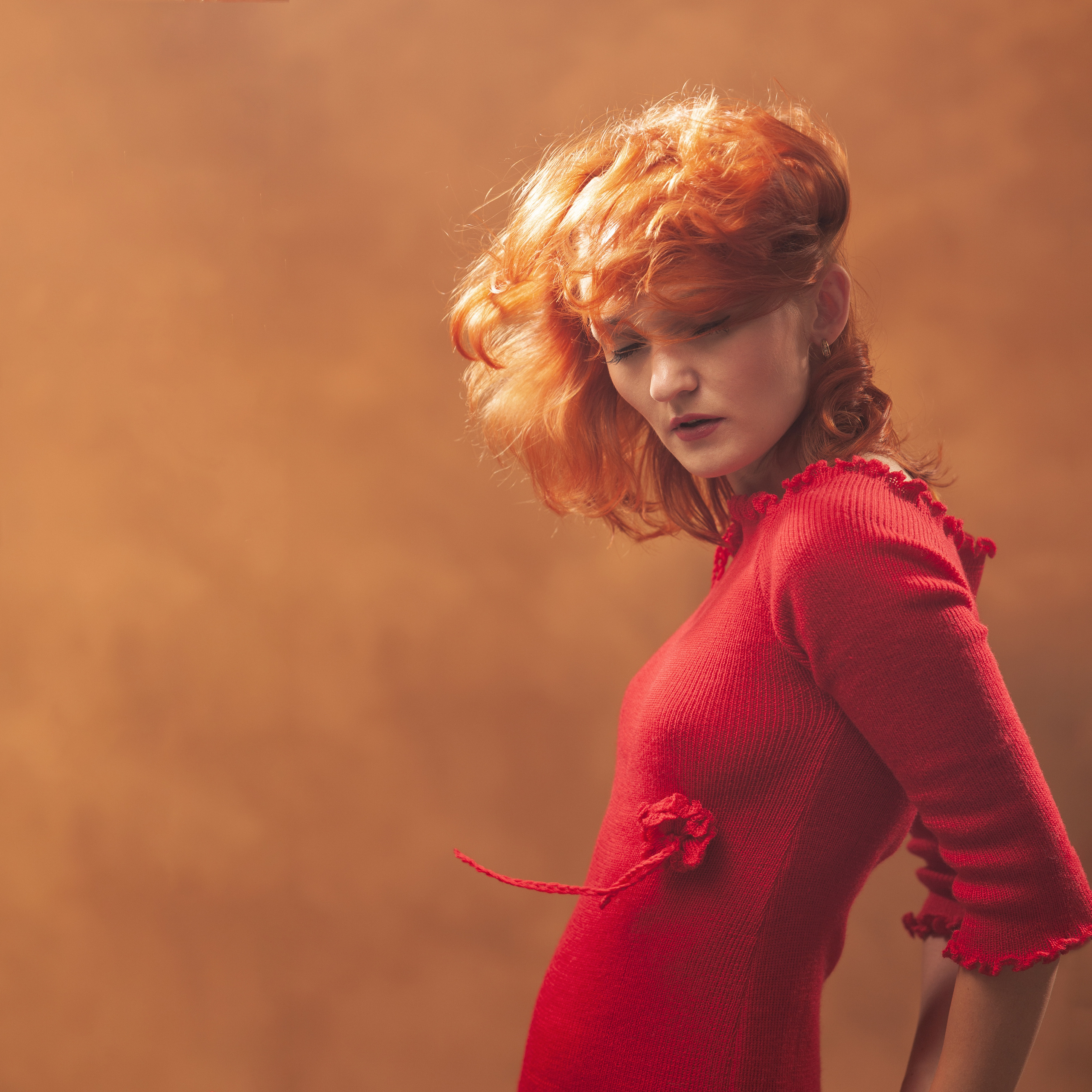 Рыжеволосая девушка в красном платье позирует с закрытыми глазами