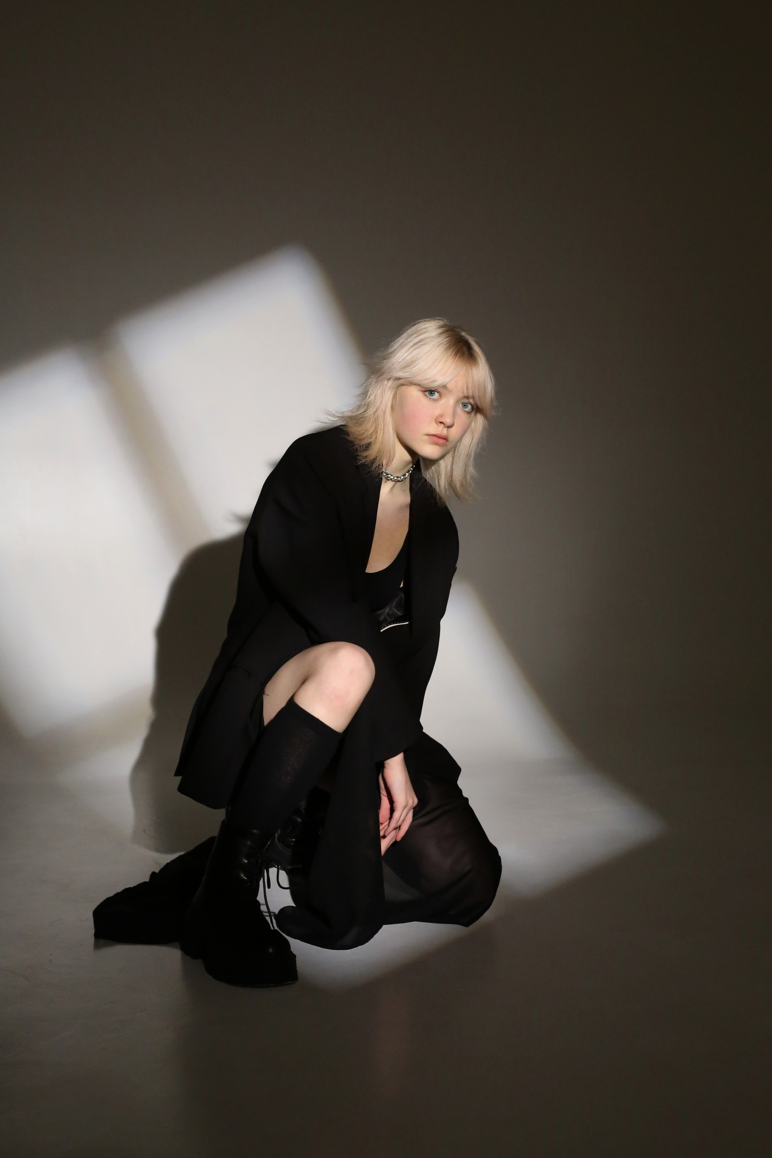 Студийная фотосессия «Геометрия»: девушка в черном костюме сидит на полу в лучах света