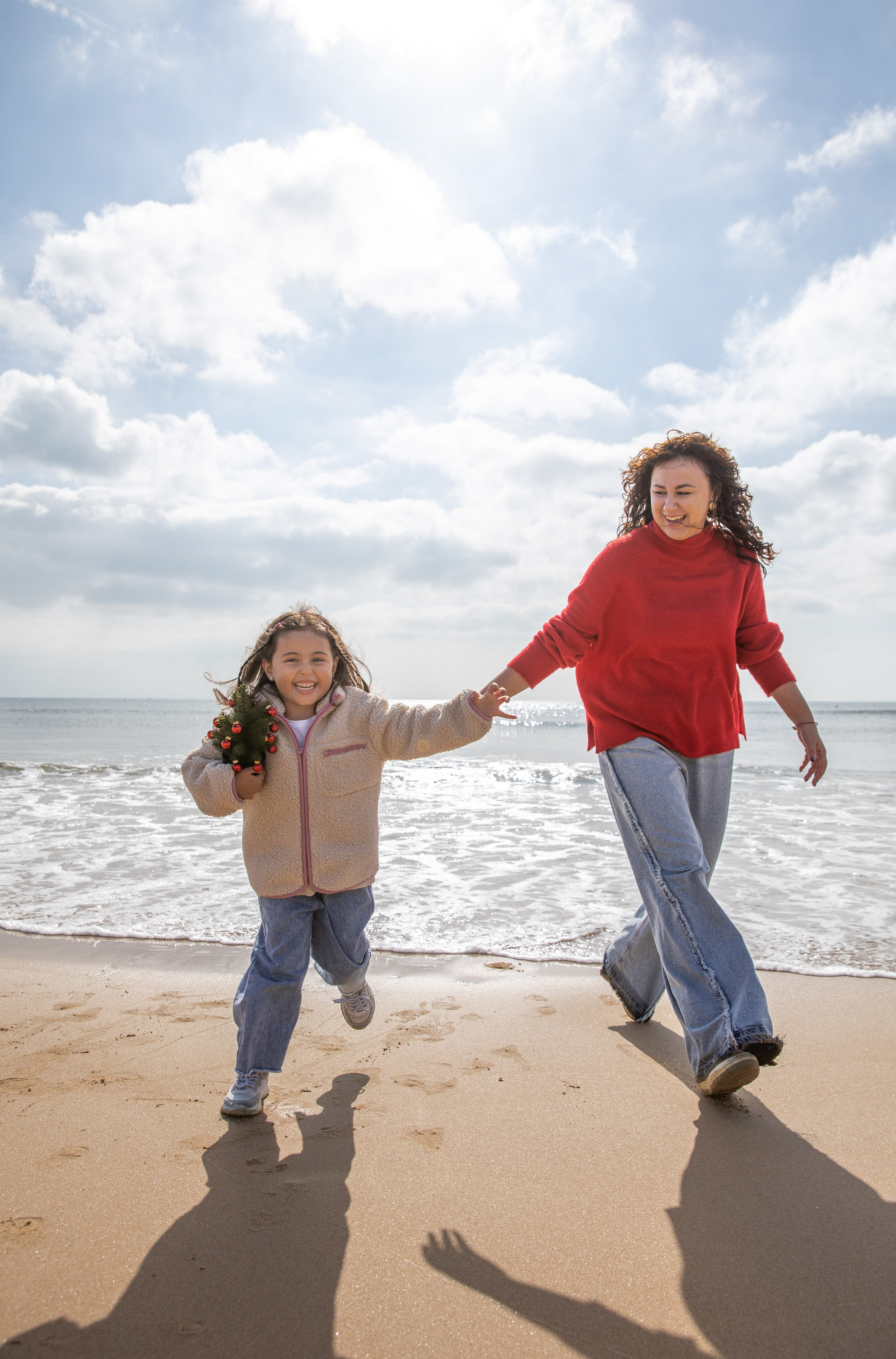 The family laughing together, as they enjoy a fun and carefree moment on the beach. Mother and daughter holding hands, their footprints left behind in the soft sand