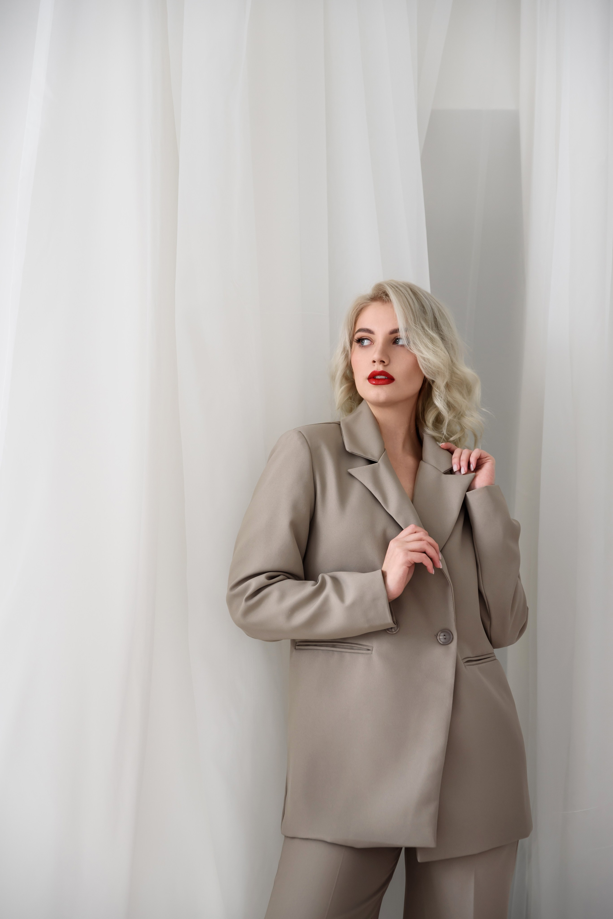 блондинка с красными губами в бежевом костюме на бежевом фоне