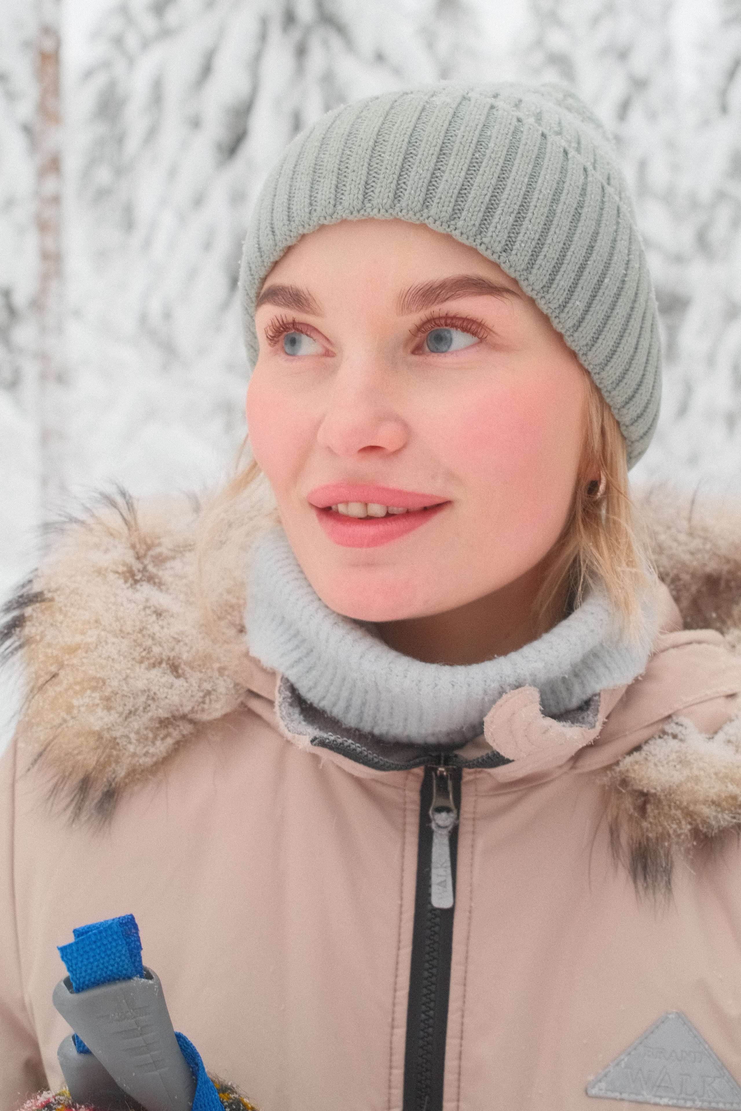 Портрет девушки с голубыми глазами в вязаной шапке в зимнем лесу