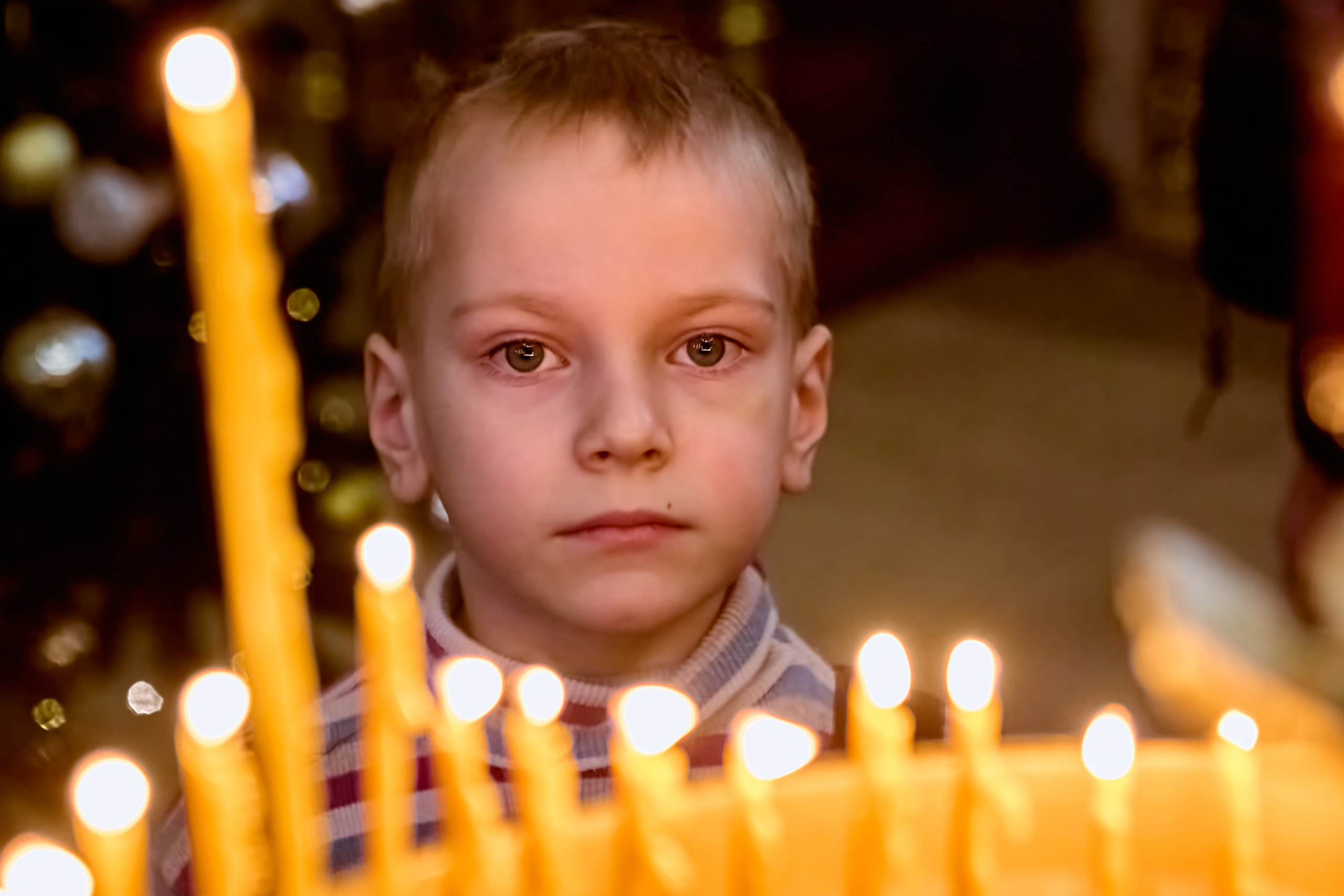 Малыш 4-6 лет возжег свечу на праздничном подсвечнике и смотрит на свечи