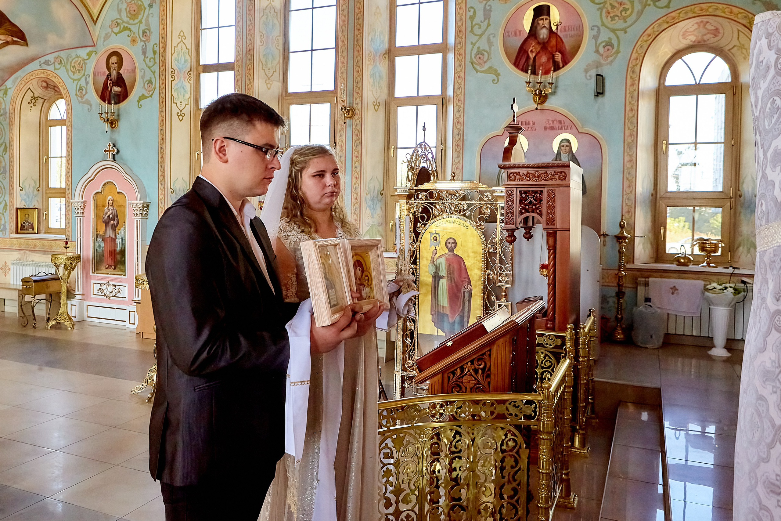 Молодые  с иконами Иисуса Христа и Богородицы стоят перед амвоном 