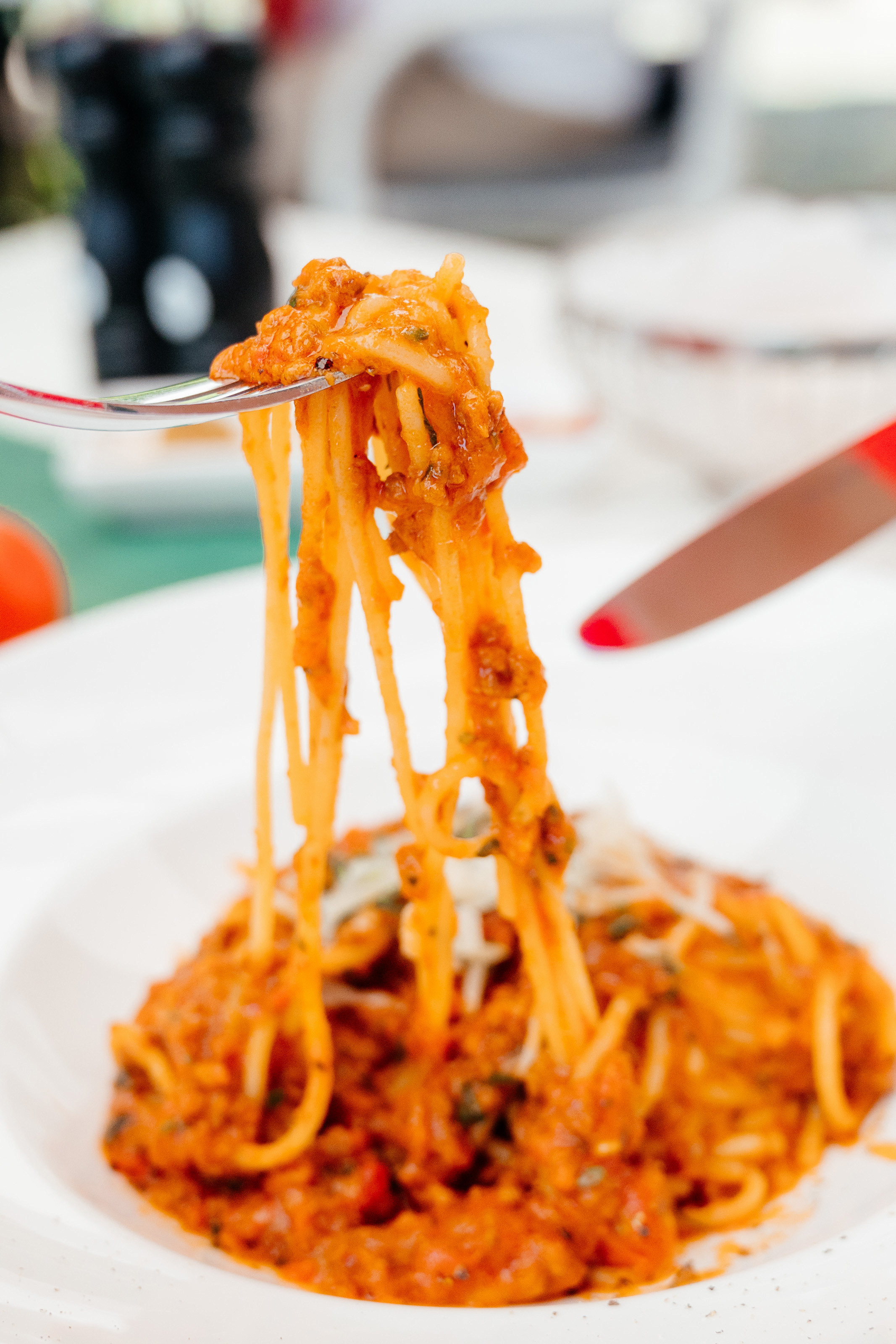 Итальянская паста в белой тарелке на вилке, нож справа