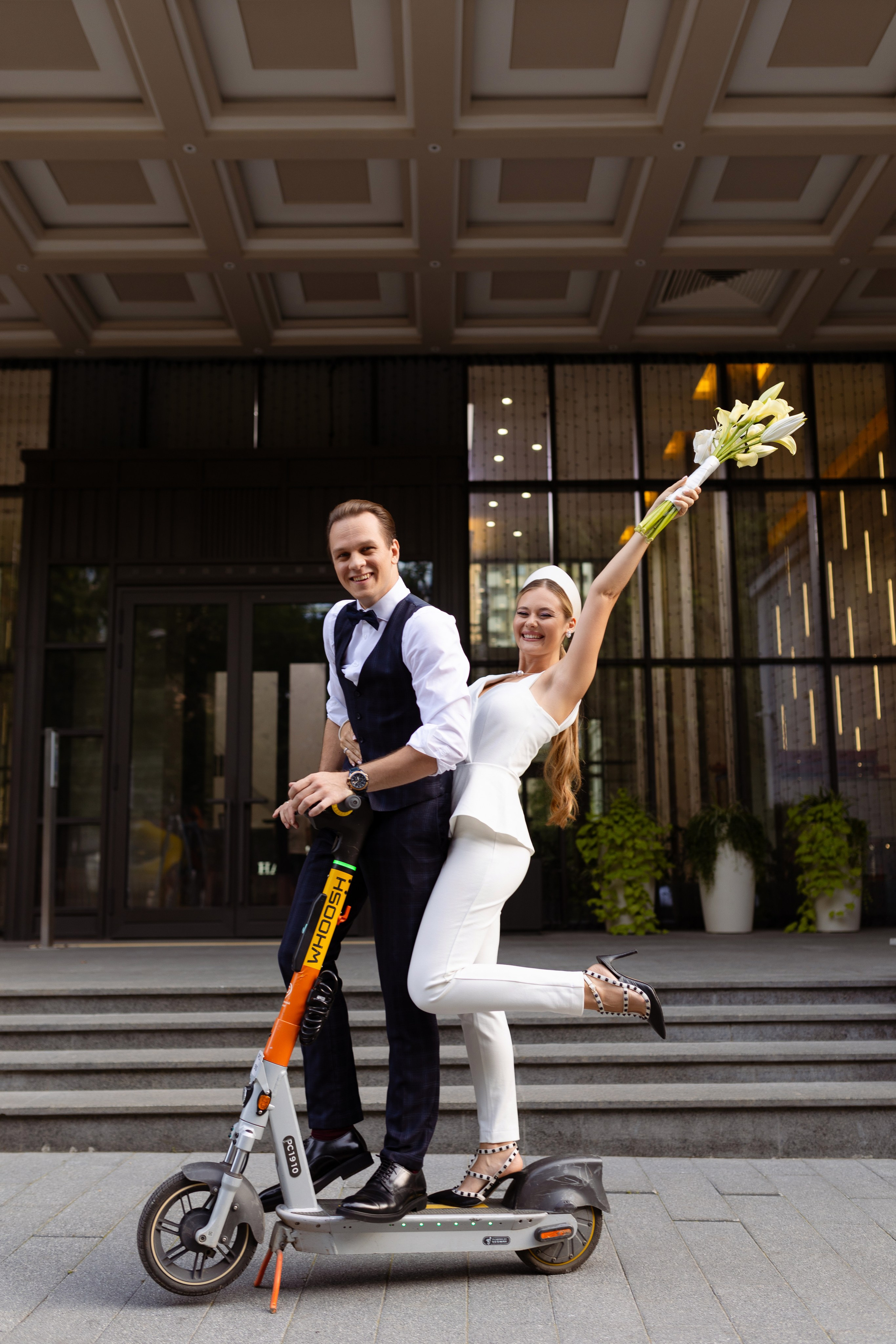 Молодые на самокате на фоне стеклянной стены.