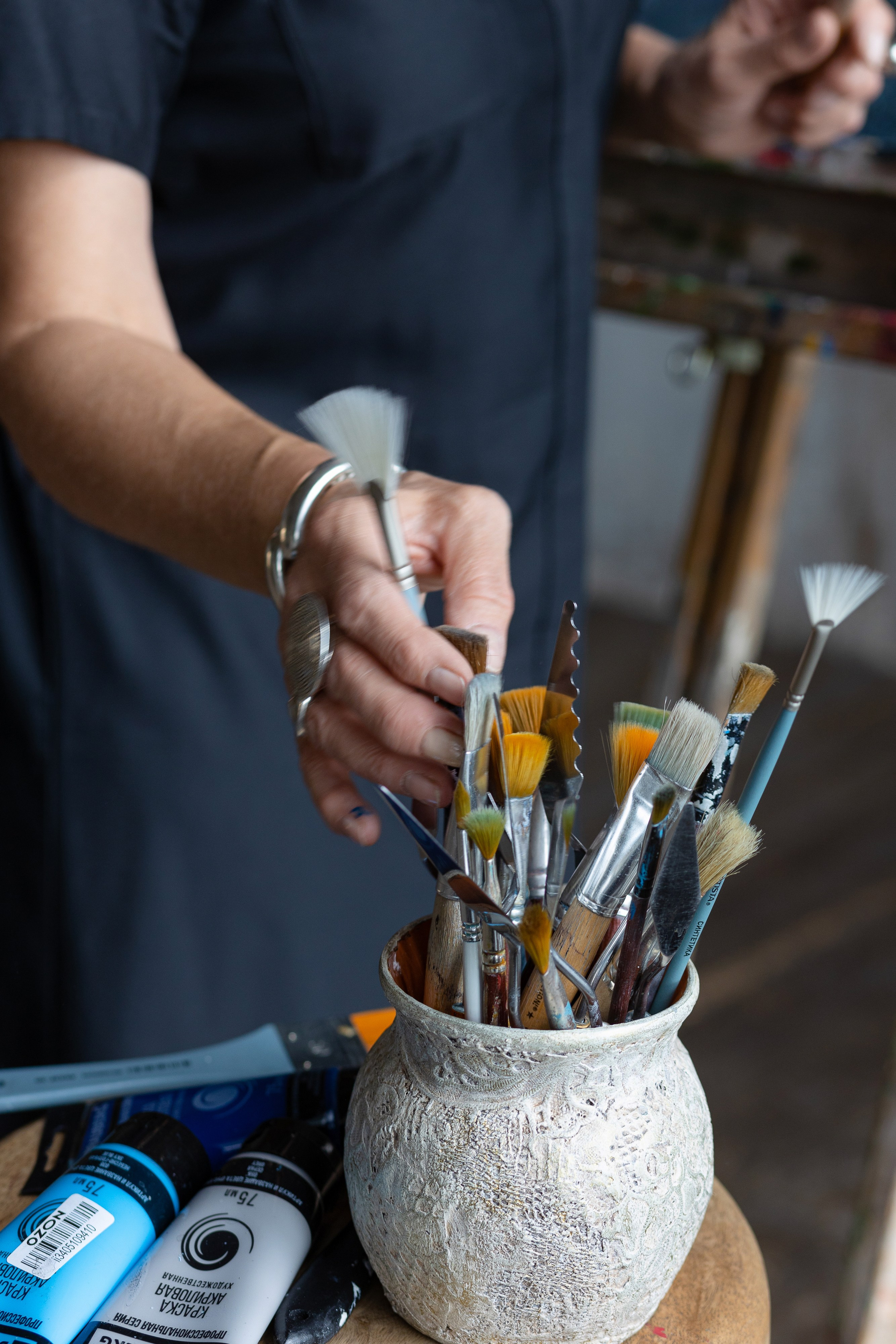 На фотографии рука художницы, которая выбирает кисть для рисования.