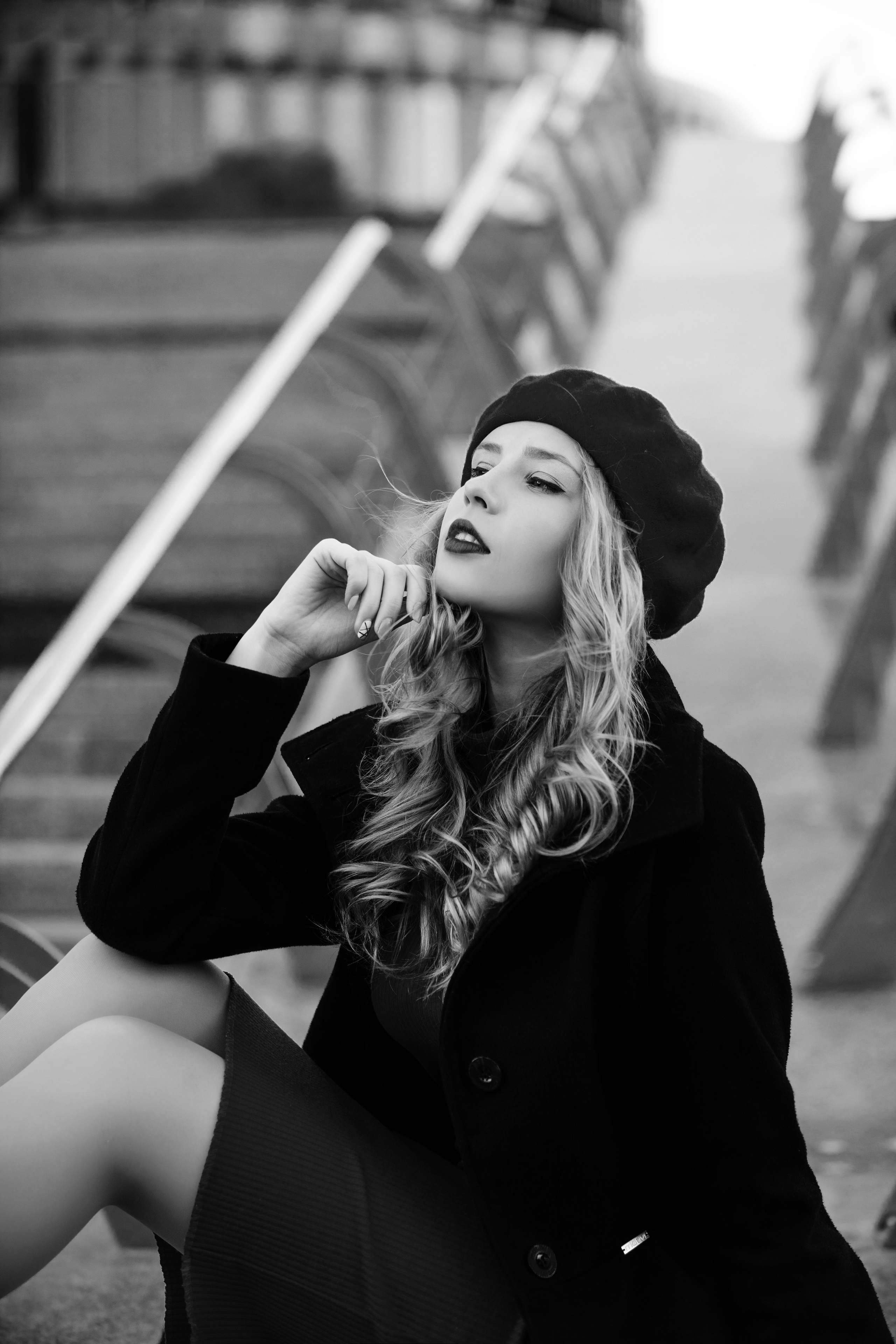 Молодая девушка в чёрном пальто и берете сидит на ступеньках Москва-Сити