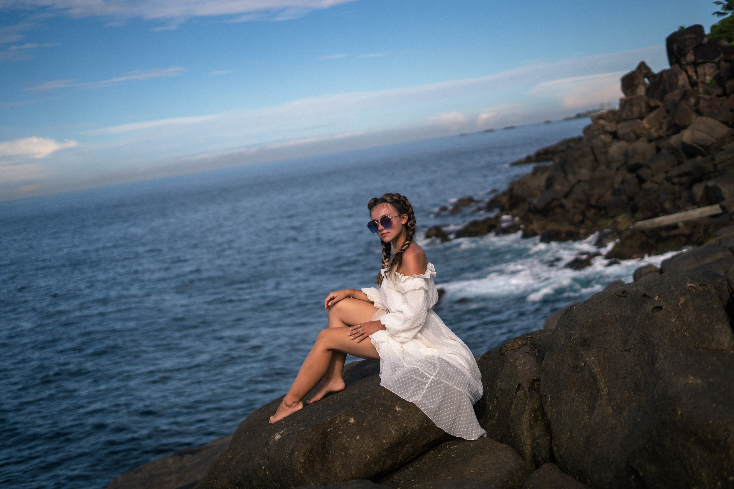 a young girl in a white dress and glasses enjoying the moment on the rocks