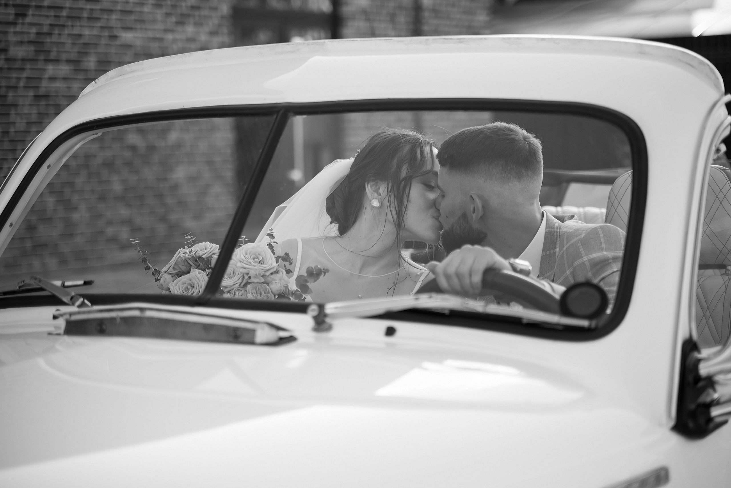 Жених и невеста целуются в ретро-автомобиле.