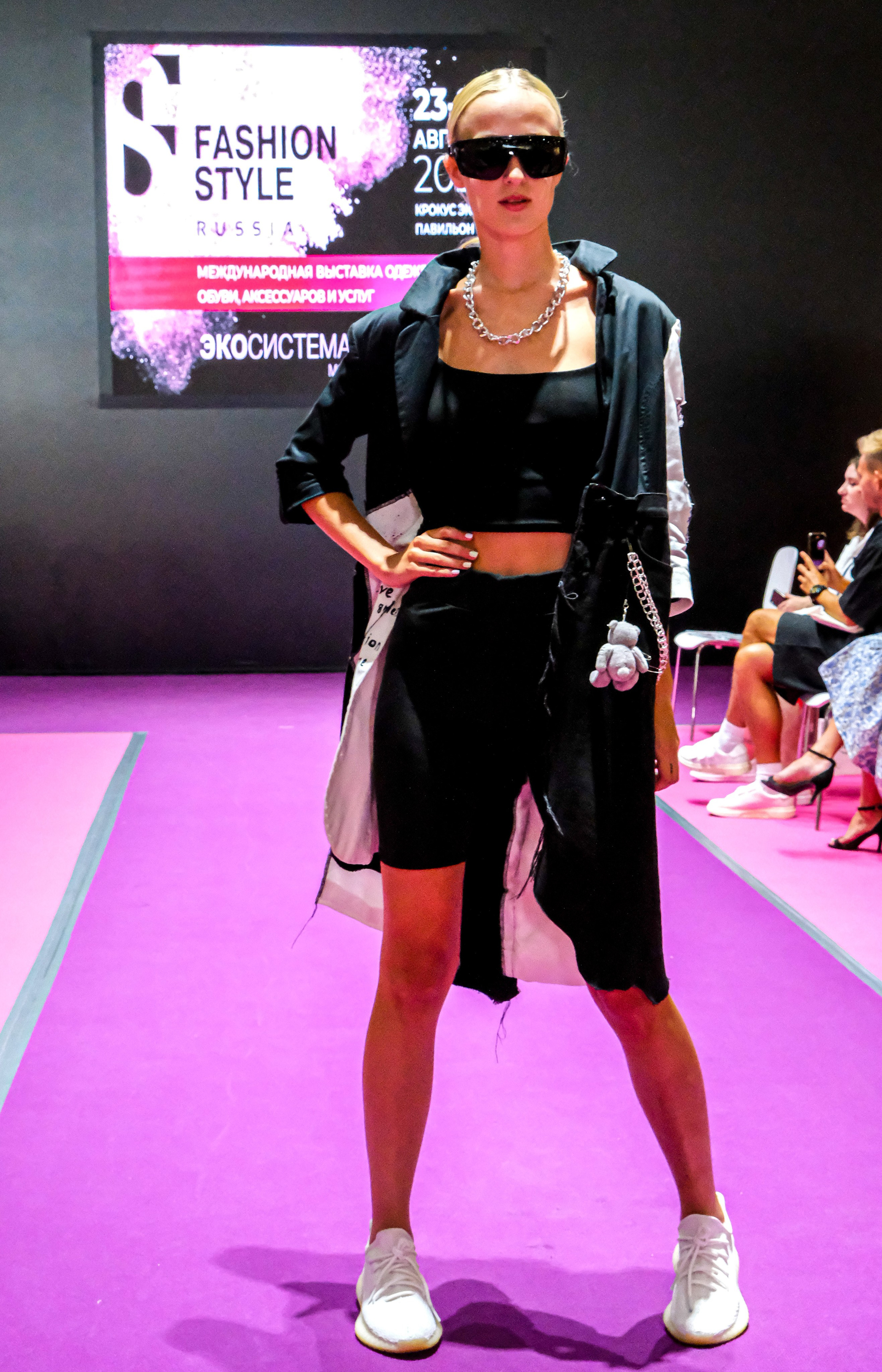  "Модели в ярких нарядах проходят по подиуму во время показа мод, освещенные яркими софитами и окруженные восторженными зрителями."