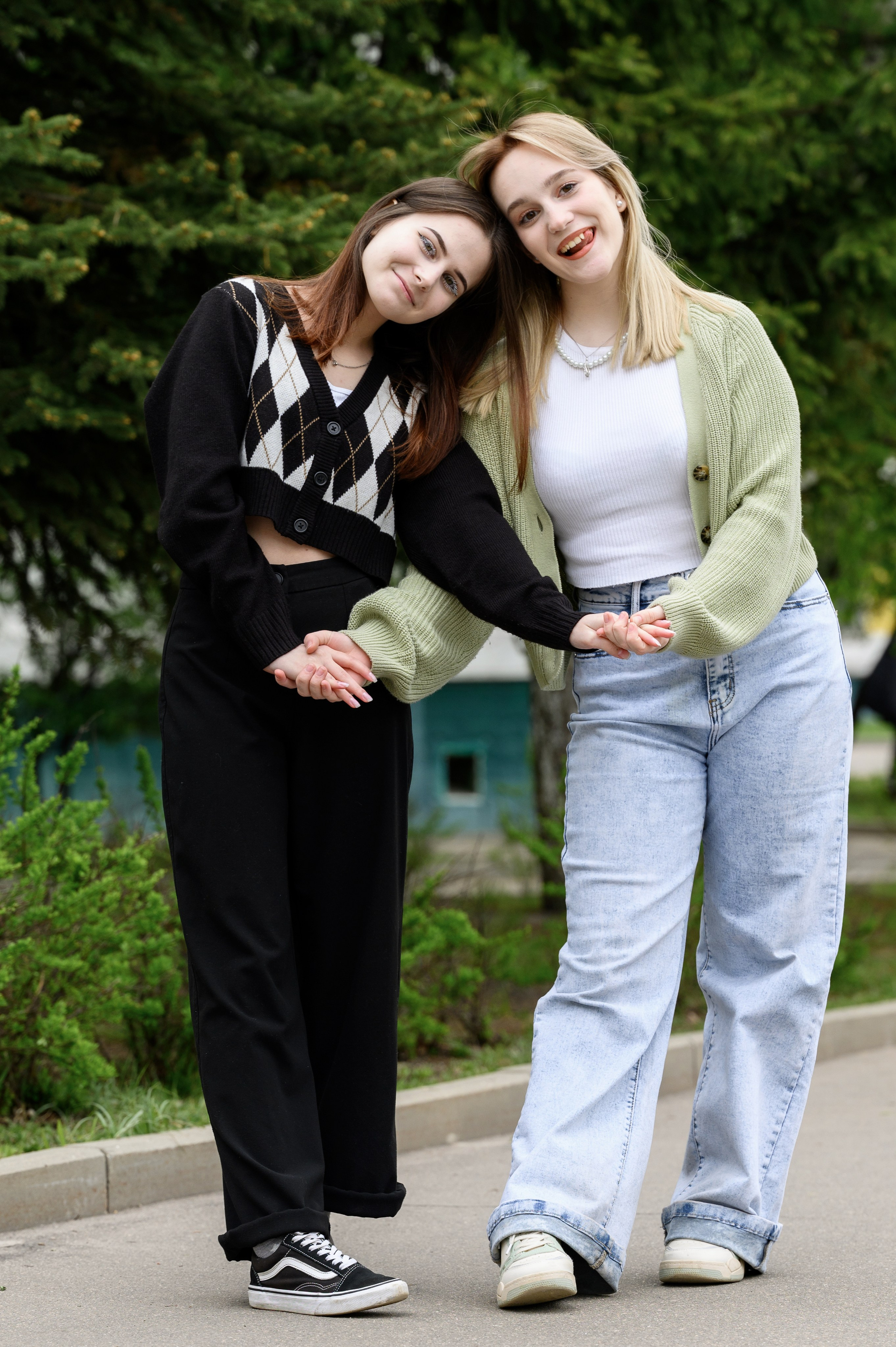 Две подруги на прогулке в парке позируют в полный рост на фоне зелени.