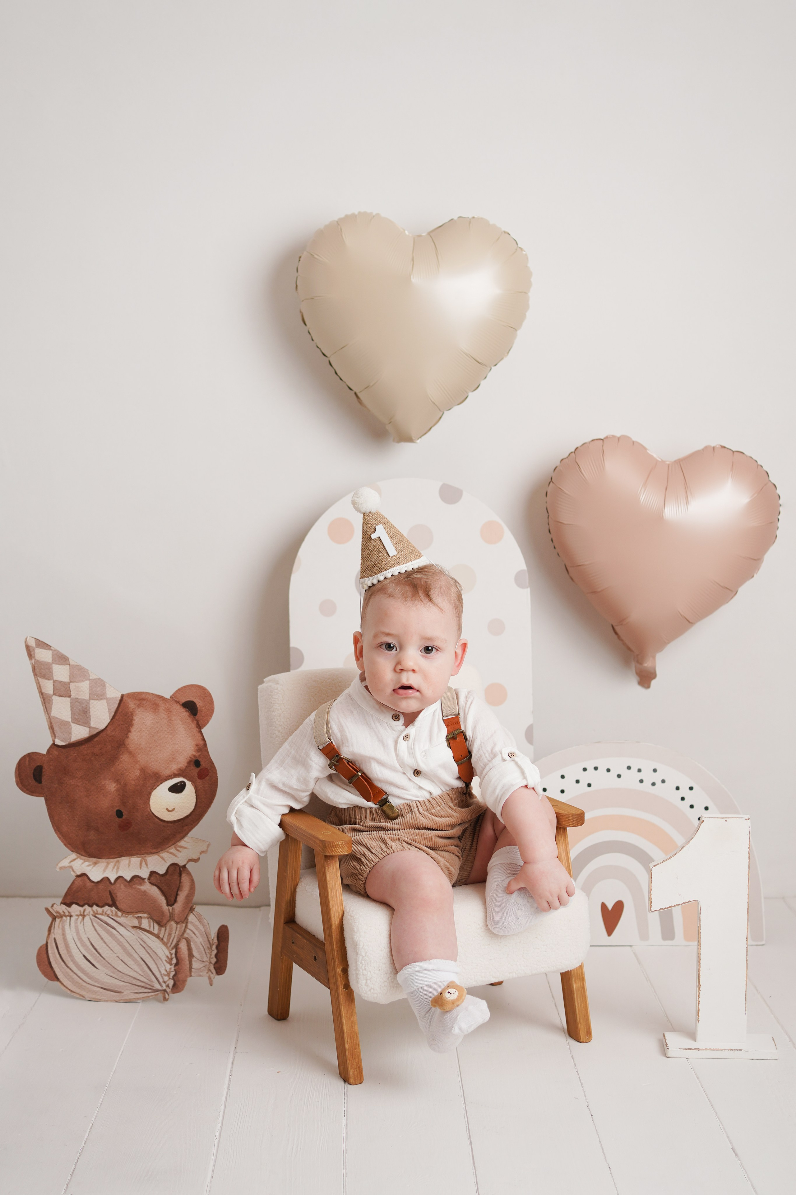 Малыш в нарядном костюме и колпачке  сидит на красивом стульчике.  Рядом фигурка мишки и единичка.