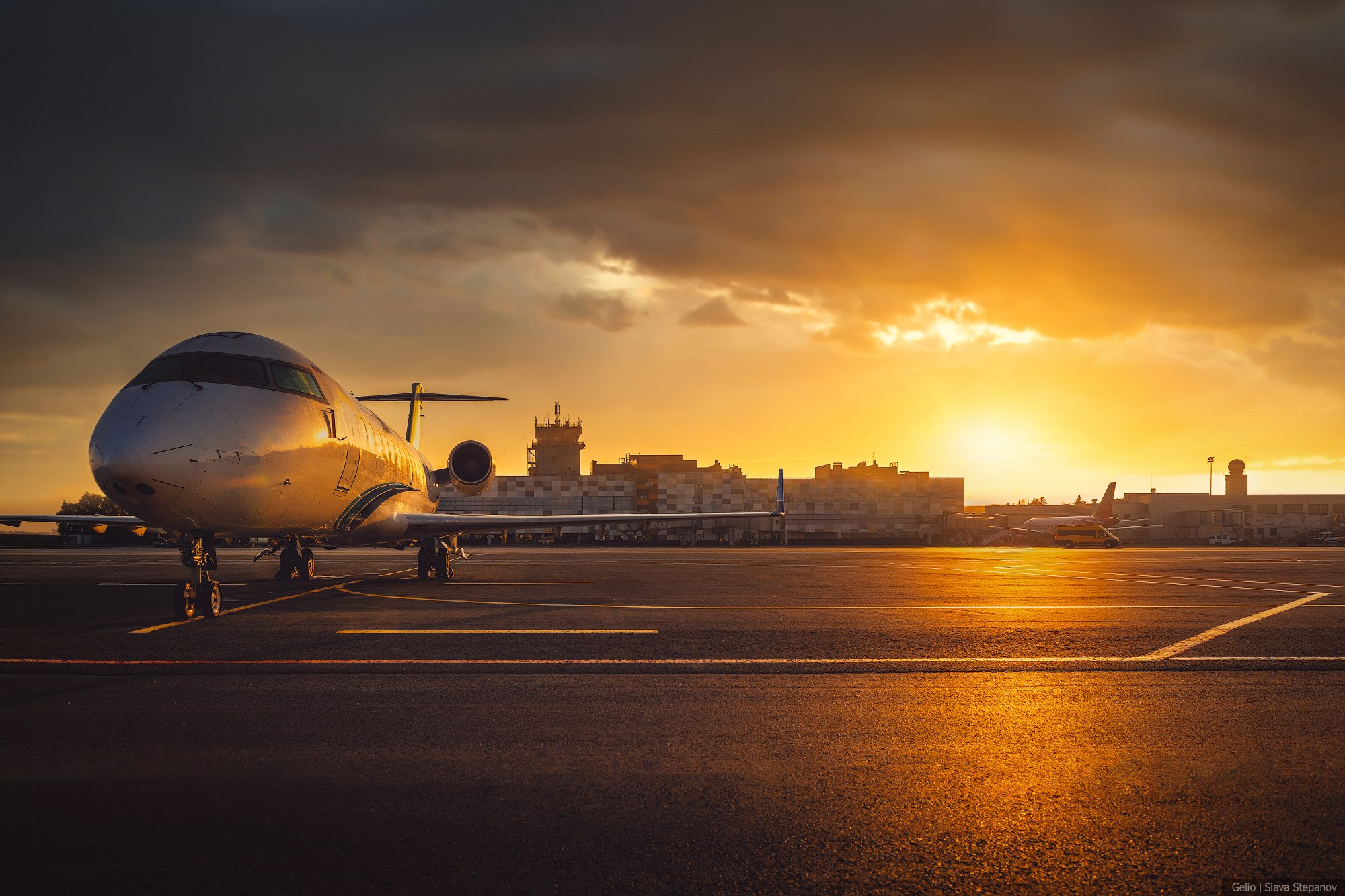 Ближнемагистральный пассажирский самолет Bombardier CRJ-200 на перроне на фоне здания аэровокзала с диспетчерской вышкой. Съемка в режиме заката с отражением на асфальте. Фотограф — Slava Stepanov.